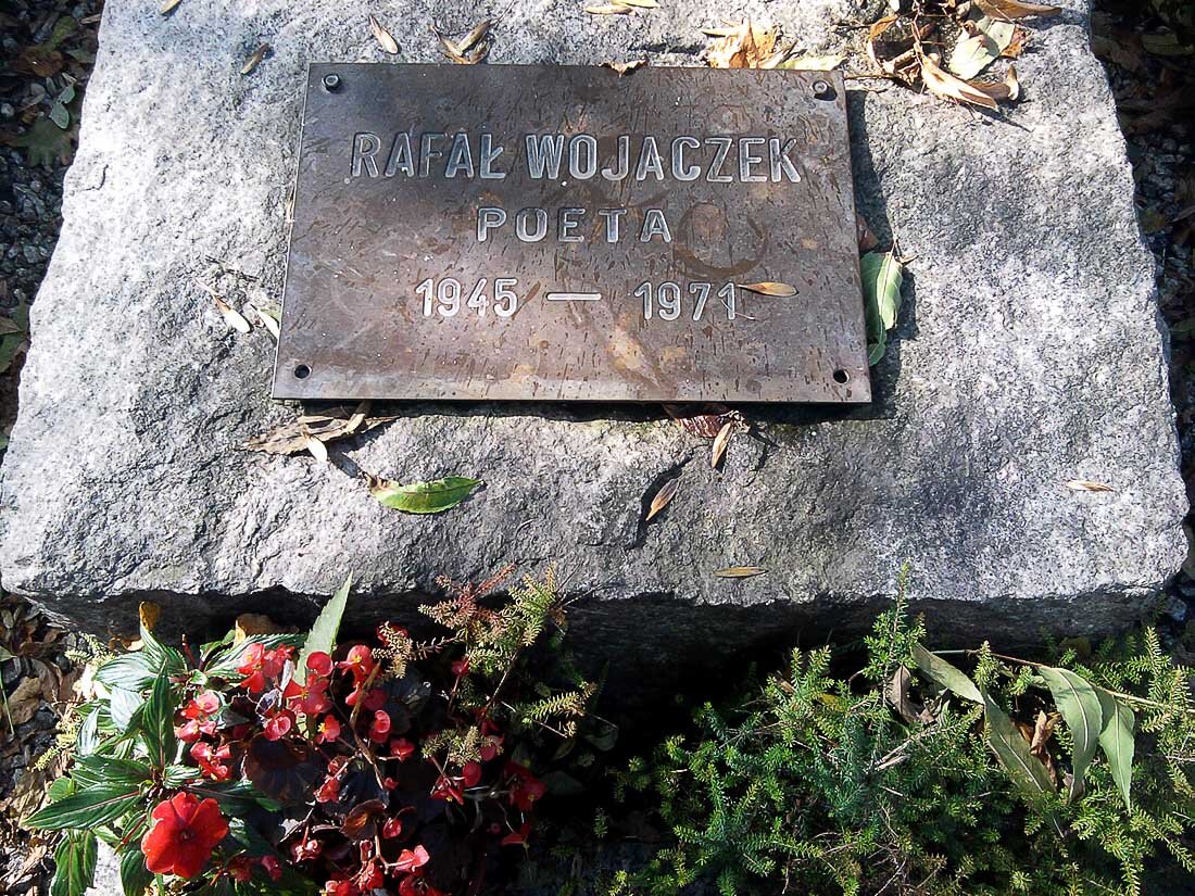 Zdjęcie przedstawia metalową tablicę. Tablica jest umieszczona na kamieniu. Na tablicy jest napis Rafał Wojaczek. Poeta. 1945 1971.