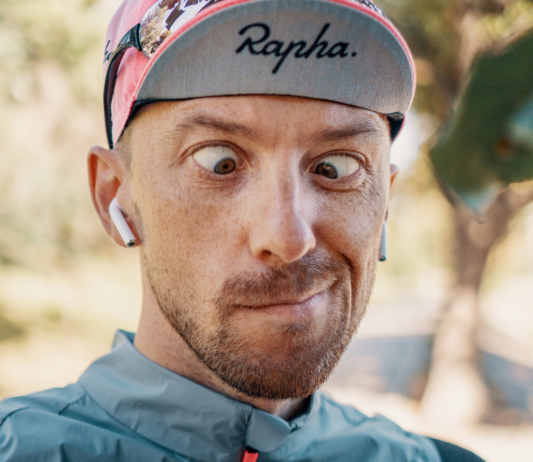 Zdjęcie przedstawia mężczyznę robiącego zeza. Ujęcie ukazuje go od ramion w górę. Na głowie ma czapkę, której daszek jest lekko wywinięty do góry, a na jego wewnętrznej stronie jest napis "RAPHA". 