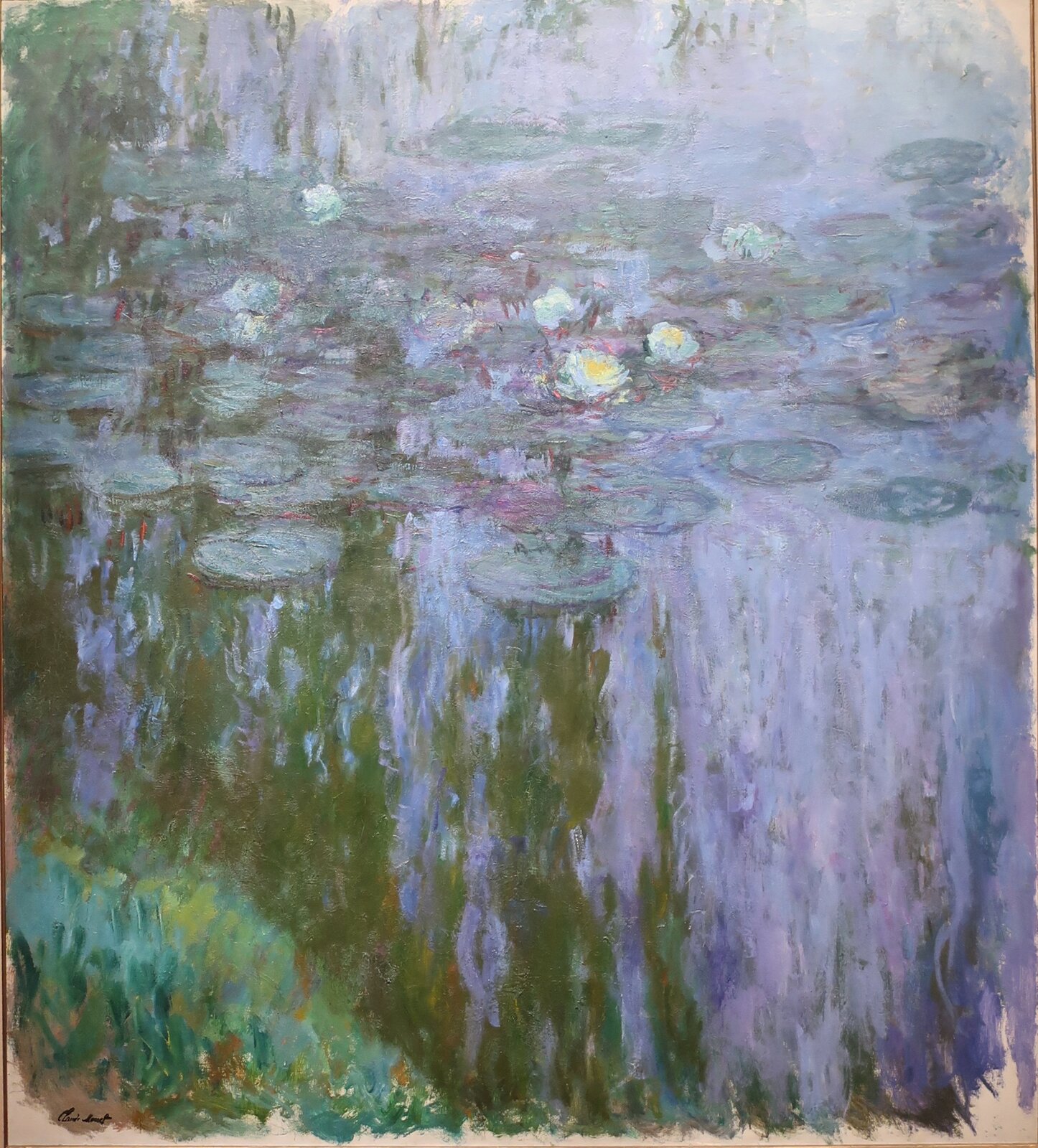 Obraz autorstwa Claude Monet, pod tytułem „Lilie wodne”. Obraz przedstawia żółto‑zielone lilie wodne, które otaczają zielone liście. W tafli wody odbija się niebieskie niebo. 