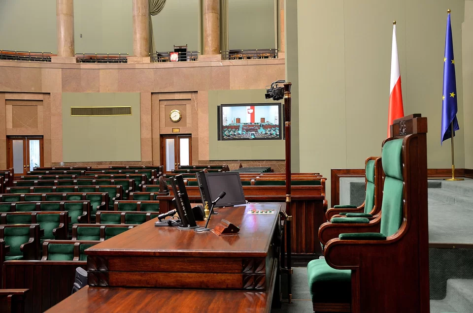 Kliknij żeby powiększyć Na zdjęciu przedstawiona jest sala obrad Sejmu RP. Na pierwszym planie znajduje się stanowisko pracy marszałka Sejmu Rzeczypospolitej Polskiej, fotel marszałka. Po prawej stronie dwie stojące na stojakach flagi: Polski i Unii Europejskiej.