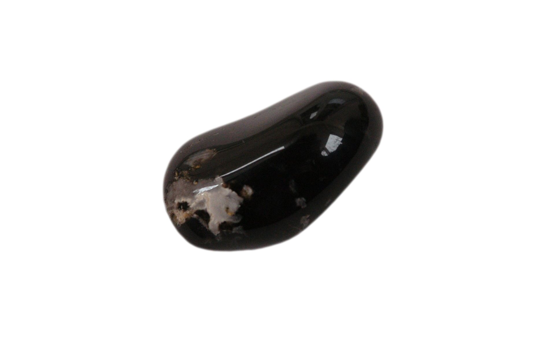 Zdjęcie przedstawia prawie idealnie czarny, gładko oszlifowany onyks w postaci lekko wydłużonej, przypominającej kształtem fasolę lub orzech nerkowca. Lewa dolna strona kamienia biała.