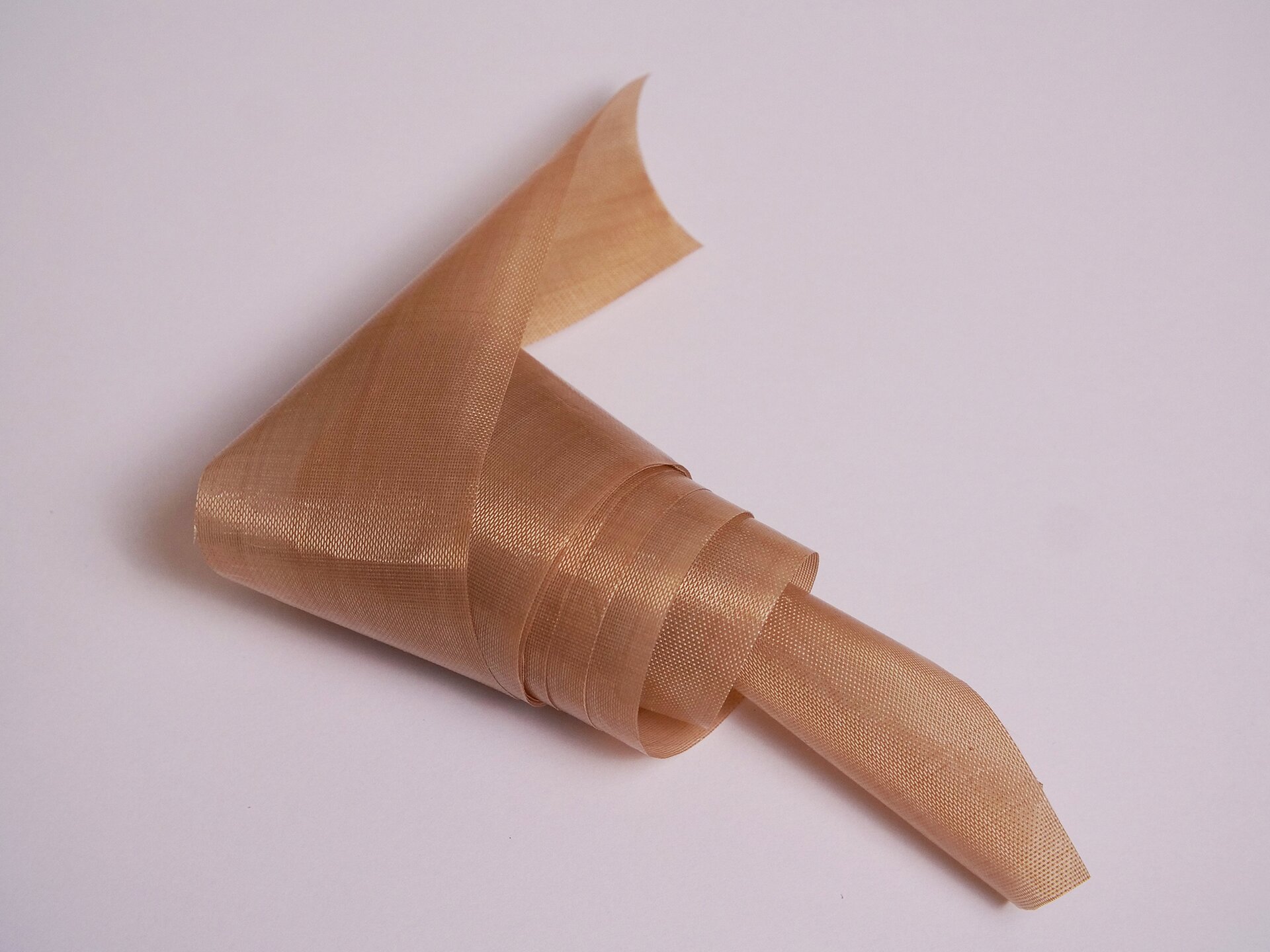 Zdjęcie przedstawia kawałek taśmy teflonowej. Materiał jest zwinięty w rulon. Ma niedużą szerokość i jest koloru brązowego. Teflon lekko połyskuje.