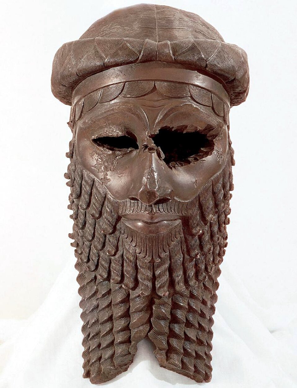 Ilustracja w kształcie pionowego prostokąta przedstawia głowę akadyjskiego władcy.  Rzeźba ukazana jest na jasnym tle. Ma długą, kręconą brodę i wąsy, a wokół głowy zapleciony gruby warkocz. Czoło okala opaska, spod której wystają półkoliste pukle włosów. Usta władcy są lekko uśmiechnięte. Oczodoły są puste. Lewy oczodół jest uszkodzony.