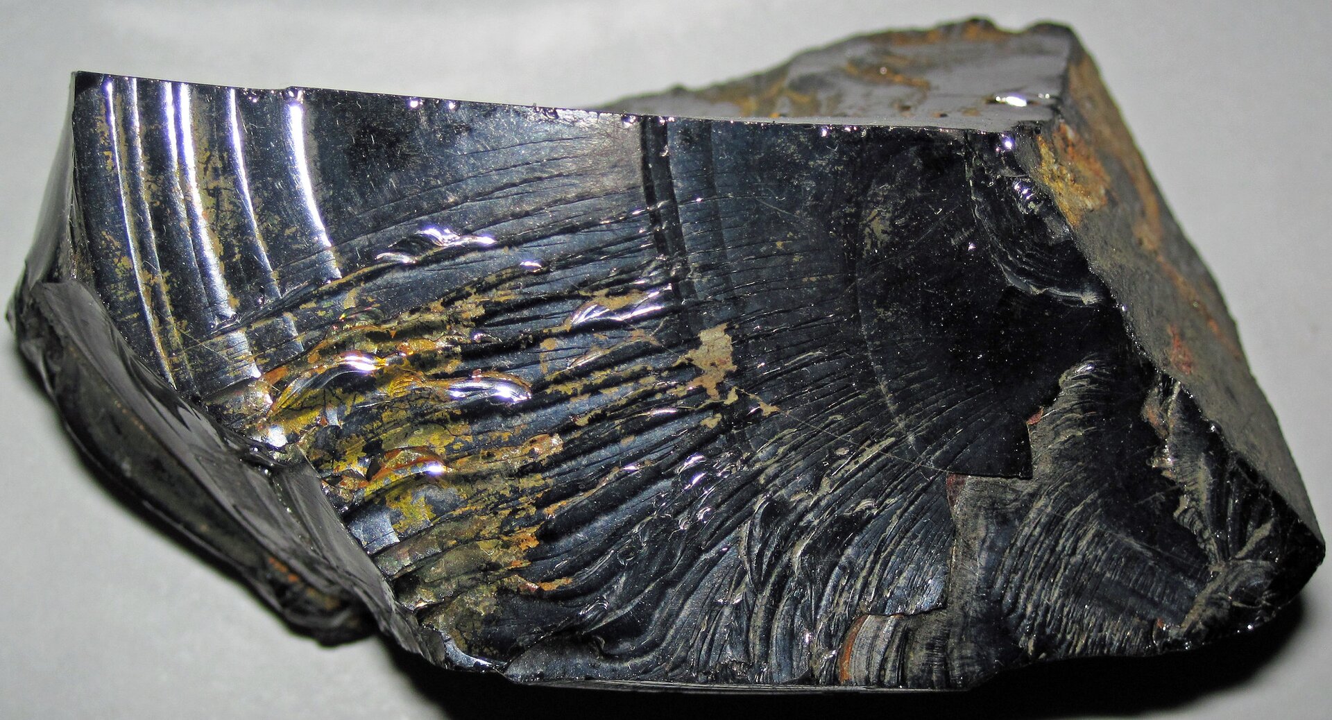 Ilustracja przedstawia kawałek szungitu. Powierzchnia minerału ma barwę czarną i błyszczącą, miejscami widoczne są brązowe przebarwienia powodowane najprawdopodobniej domieszkami innych minerałów. Cechą charakterystyczną jest wyżłobiona powierzchnia, będąca powodowana przełamem muszlowym tego rodzaju węgla.