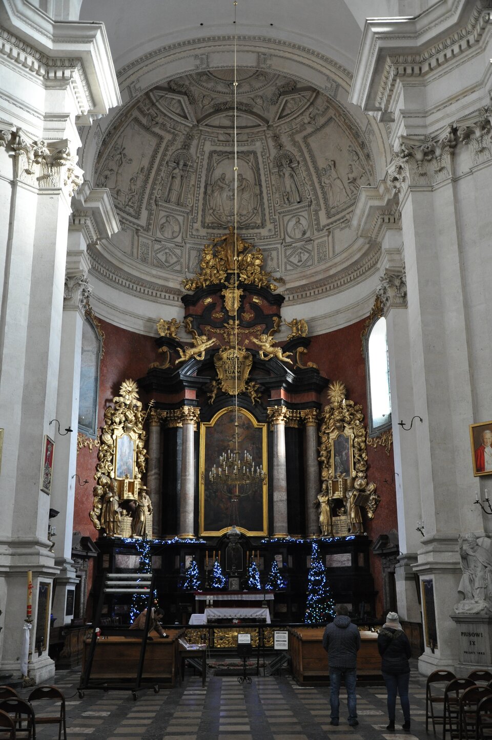 Ilustracja przedstawia wnętrze Kościoła pw św. Piotra i Pawła ze zbliżeniem na późnobarokowy ołtarz główny z rzeźbami Antoniego Frączkiewicza. Obraz w ołtarzu „Wręczenie kluczy św. Piotrowi” namalował około 1820 roku Józef Brodowski. Wszystkie ściany kościoła są białe oprócz ściany, na której znajduje się ołtarz: ma ciemno‑brązowy kolor. Ołtarz jest wykonany z czarnego marmuru i jest bogato zdobiony złotymi elementami. Ciemna ściana za ołtarzem wraz z ołtarzem stanowi wyraźny kontrast z jasnym wnętrzem. 