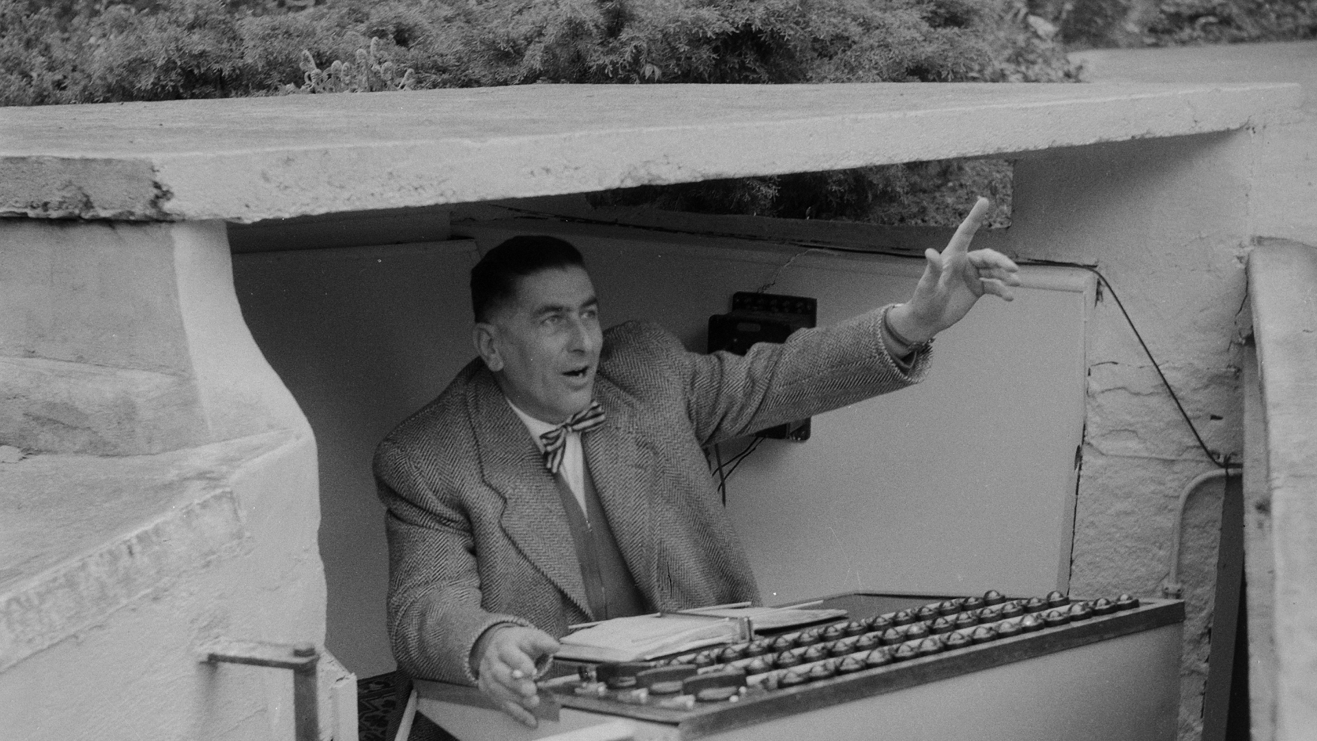 Zdjęcie przedstawia mężczyznę/suflera, który znajduje się w specjalnej budce pod sceną.Mężczyzna ma przed sobą scenariusz. Ma uniesioną rękę.