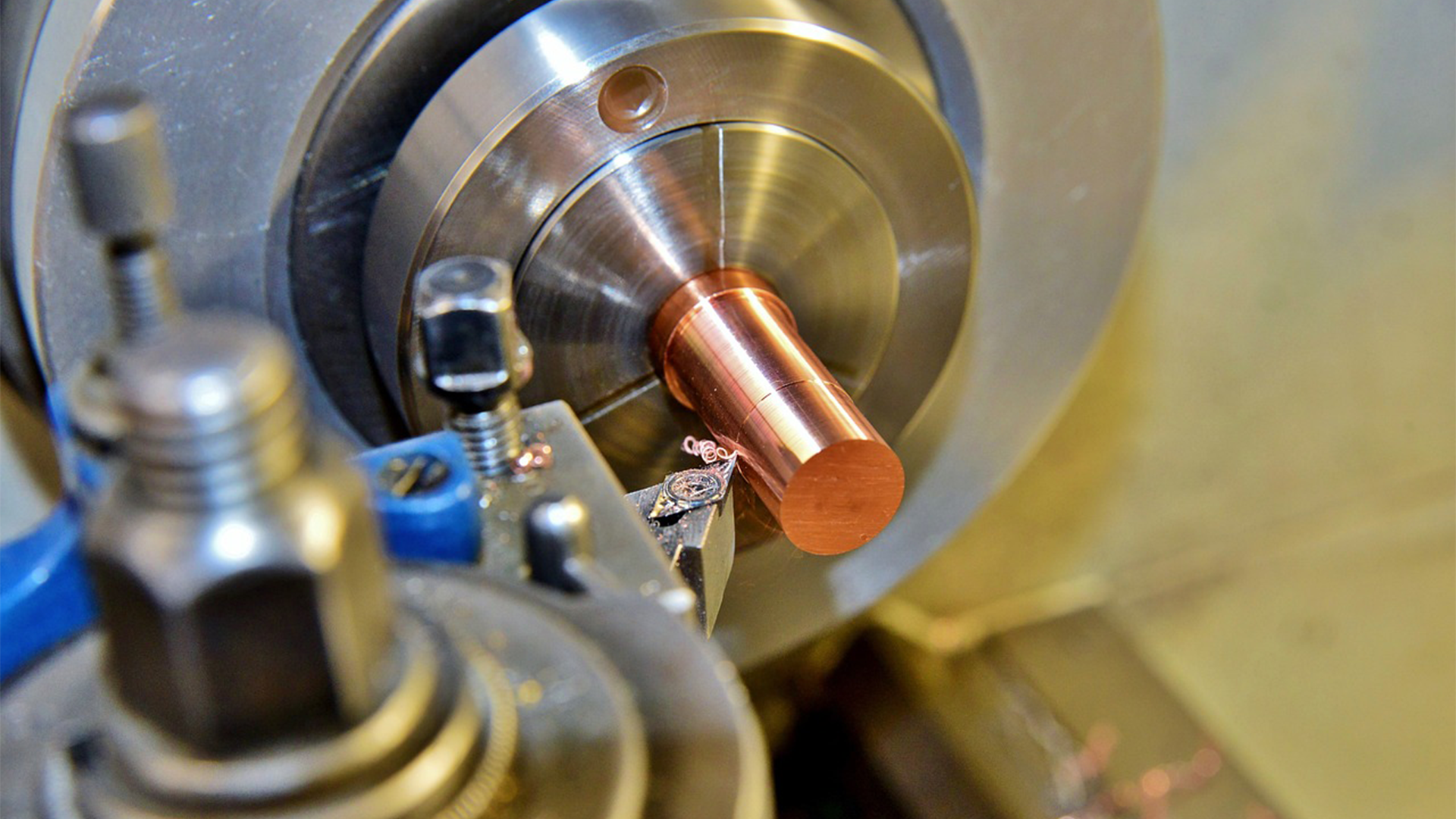 Grafika przedstawia proces toczenia. Na maszynie zamontowany jest walcowaty metal, który ulega obróbce.