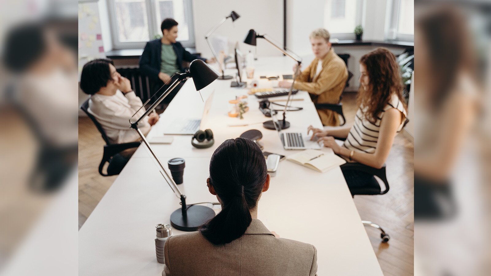 Zdjęcie przedstawia pomieszczenie biurowe. Przy biurku siedzi pięć osób i prowadzą rozmowę. Transkrypcja nagrań znajduje się poniżej.