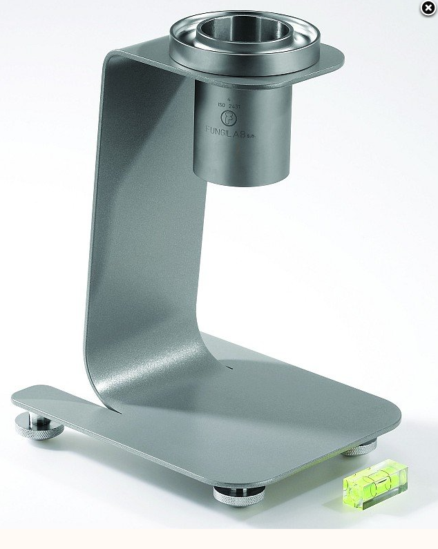 Zdjęcie prezentuje lepkościomierz wypływowy typu kubek Forda. To stalowoszare, cylindryczne naczynie zawieszone na ramieniu. Ramię osadzone jest na stabilnej podstawie umieszczonej na nóżkach.