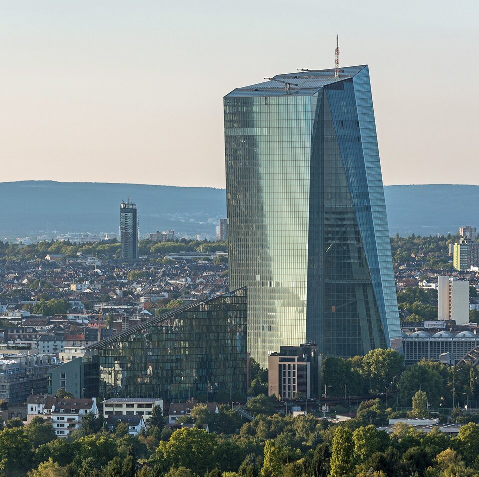Na pierwszym planie, w otoczeniu drzew, widoczny jest nowoczesny, bardzo wysoki budynek, który dominuje nad innymi zabudowaniami. Uwagę zwracają szklane fasady, obok widać mniejszy trójkątny budynek - również przeszklony. 