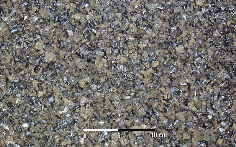 Na zdjęciu lapille– typ materiału piroklastycznego wyrzucanego podczas erupcji wulkanu. Kamyki mają kolor czarny z białym pasami, brązowy i szary. 