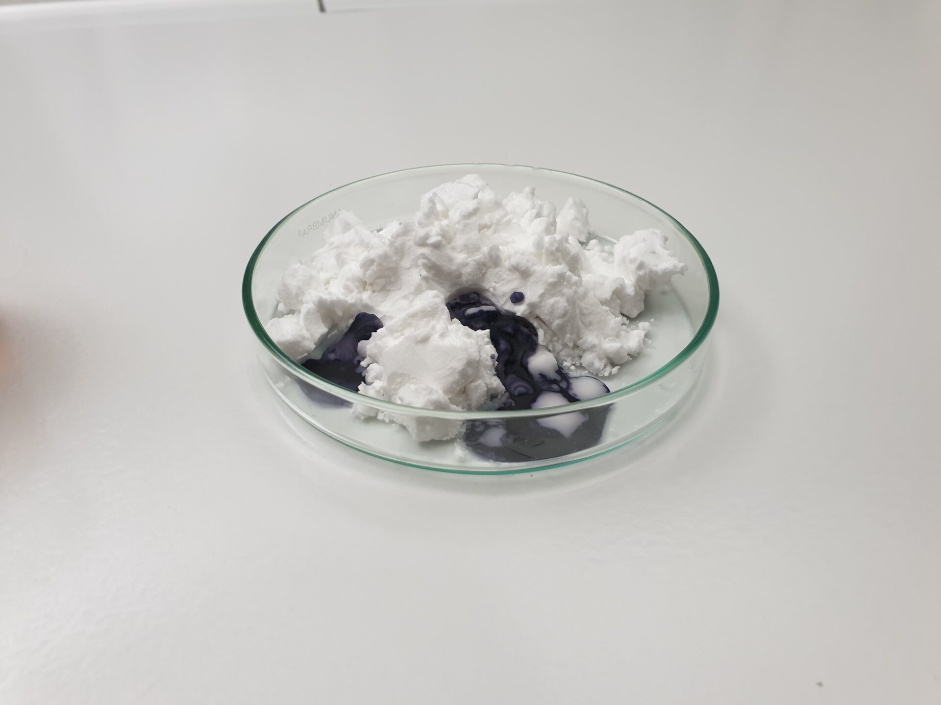 Zdjęcie przedstawia szalkę Petriego, na której umieszczono grudkę skrobi. Ma ona postać sypką i biały kolor. Pomiędzy grudkami widoczny jest niebieski, gęsty płyn. To płyn Lugola. 