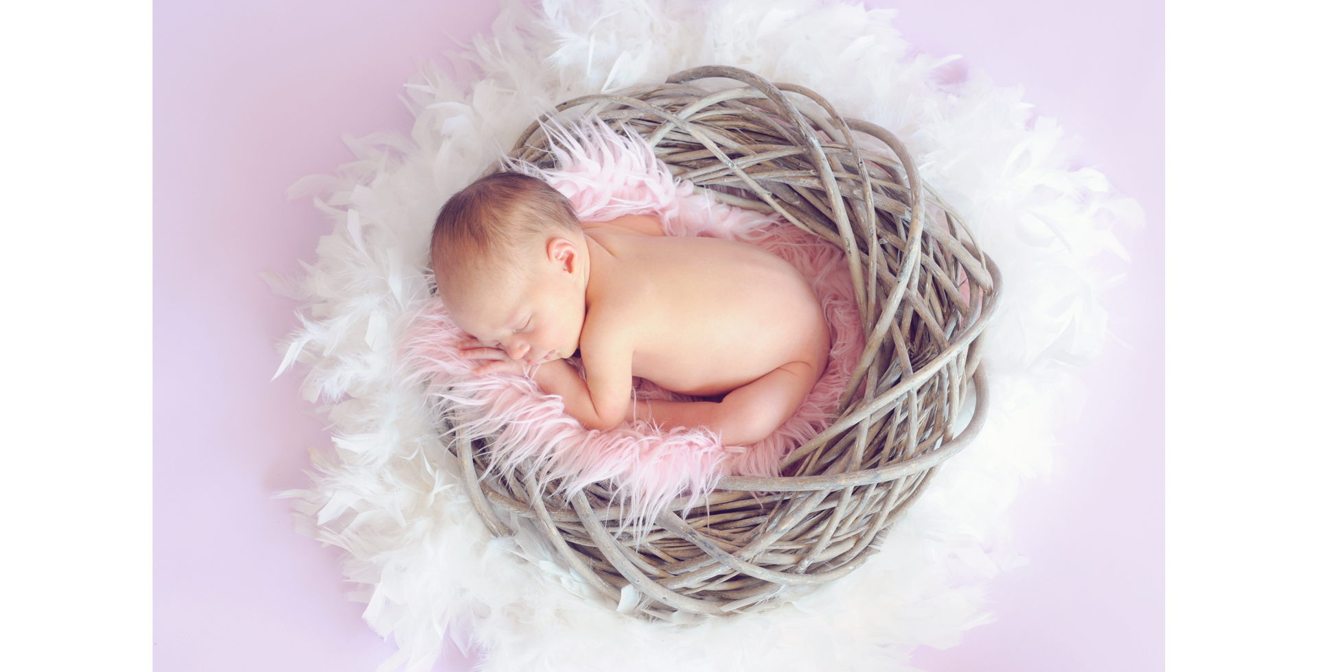 Zdjęcie przedstawia nagie niemowlę, śpiące na brzuszku w okrągłym koszyku, na długowłosym futerku. Wokół koszyka znajdują ptasie pióra.