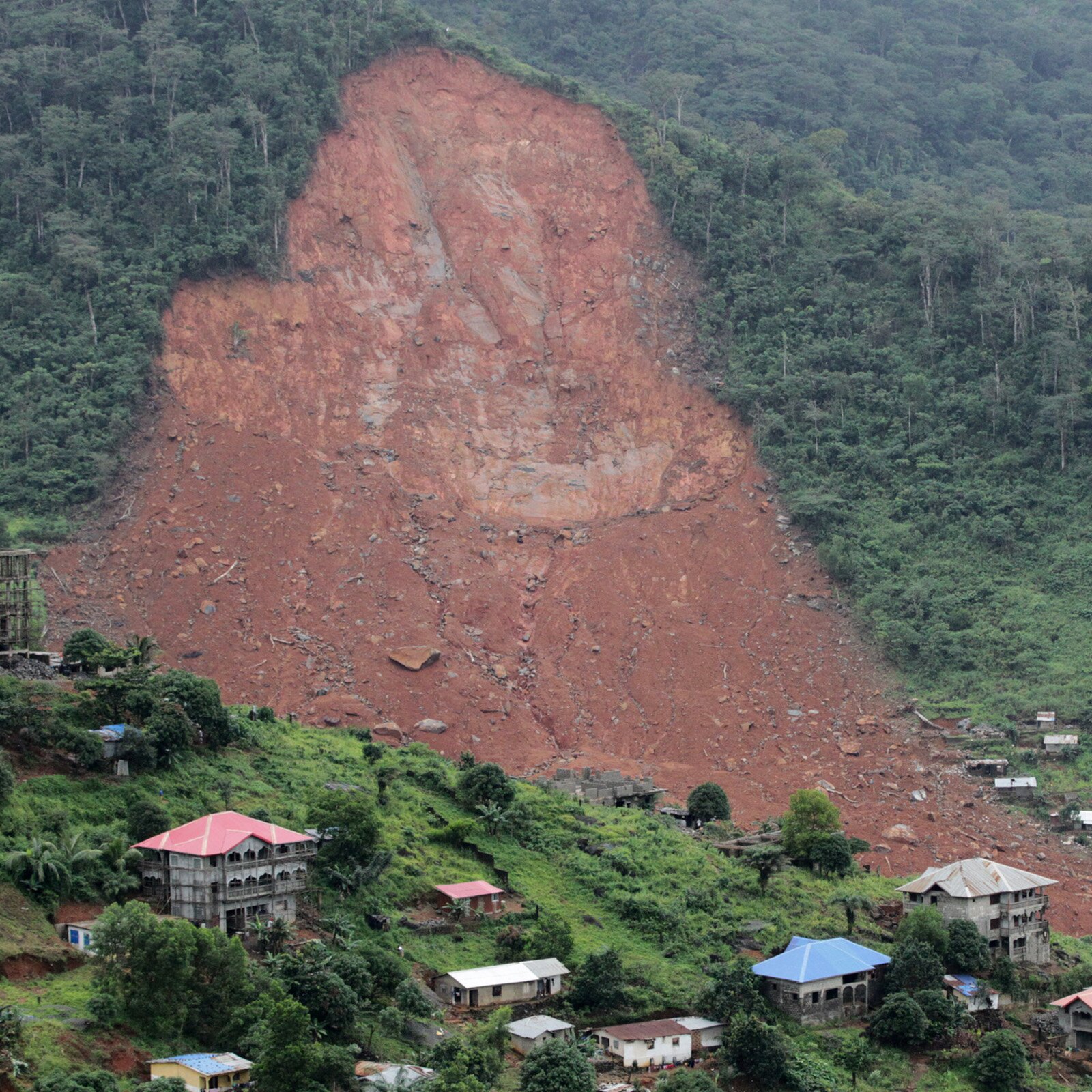 Zdjęcie przedstawia spływającą ze zbocza góry lawinę błota. W dole widoczne dachy domów.