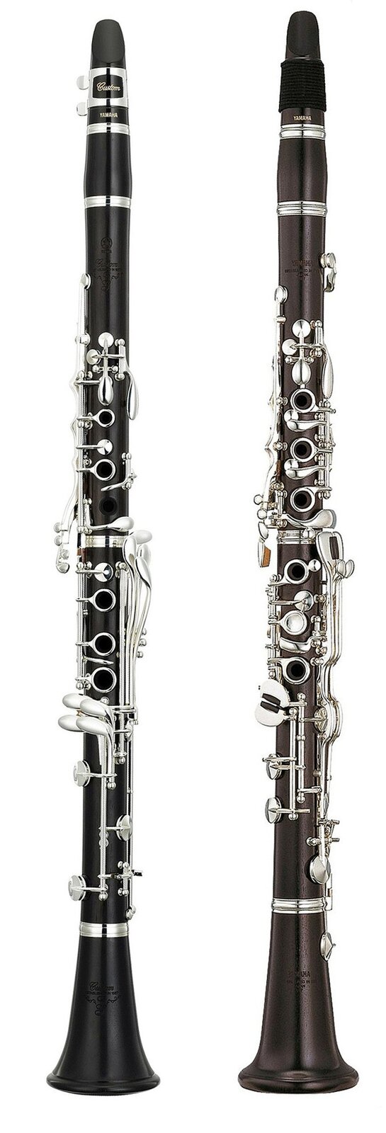 Zdjęcie przedstawia klarnet. Widoczne są dwa ujęcia instrumentu z boku i z przodu. Instrument jest przedstawiony w pionie, w postaci czarnego drewnianego podłużnego korpusu (cylindrycznej rury) z metalowymi, srebrnymi elementami, w dolnej części rozszerzający się kielichowato, co obrazuje czarę dźwiękową. W górnej części korpusu widoczny spłaszczony element – ustnik. Na powierzchni instrumentu widoczne są otwory, z których dużą część jest zamykana metalowymi klapami.