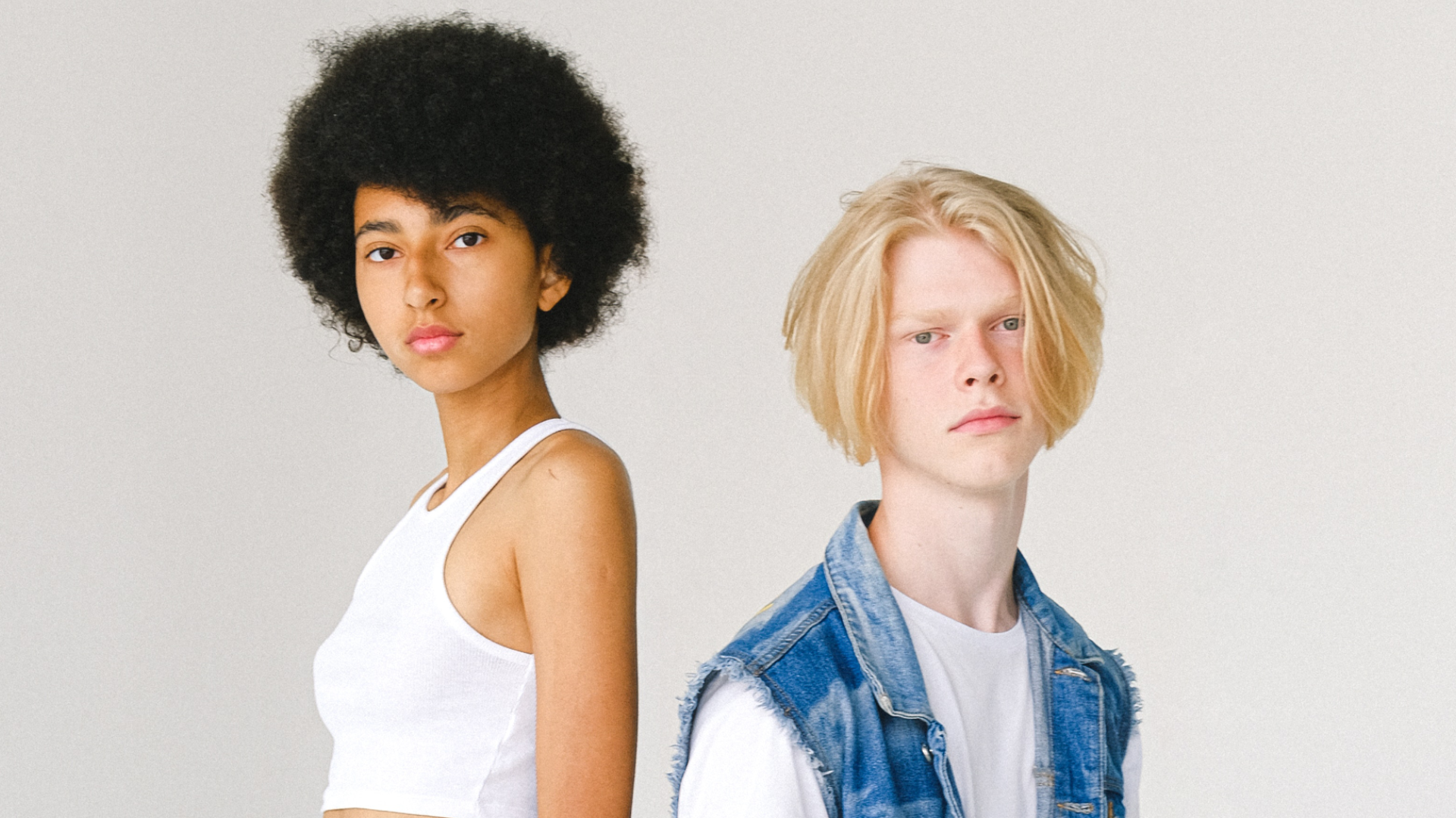 Zdjęcie przedstawia dwoje nastolatków. Po lewej stronie wysoka, chuda dziewczyna z ciemną karnacją. Na głowie ma bujne, czarne, kręcone włosy. Po prawej stronie szczupły chłopiec z dłuższymi włosami. Chłopiec jest niższy od dziewczyny.