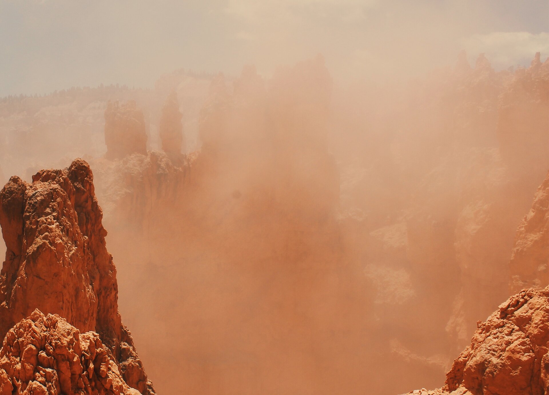 Zdjęcie przedstawia burzę piaskową zasłaniającą skały. Całość przykryta jest pomarańczowym pyłem.