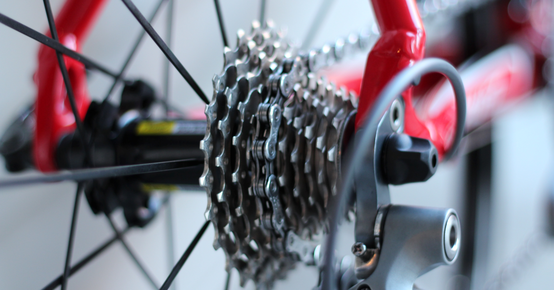 Fotografia przedstawia fragment tylnego koła roweru, głównie część z kasetą zębatek. Łańcuch spoczywa na środkowej zębatce. W tle rozmazana rama roweru.