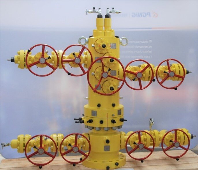 Na zdjęciu widoczna jest głowica eksploatacyjna selektywna do eksploatacji dwóch horyzontów jednocześnie. Głowica eksploatacyjna to urządzenie montowane na szczycie odwiertu, w celu zamknięcia wylotu odwiertu wiertniczego. Składa się z zaworów i otworów spustowych służących do kontrolowania odwiertu. Głowica widoczna na zdjęciu składa się z głównego trzonu. W jej dolnej części z prawej i lewej strony znajdują się przyłącza na przewody wiertnicze. Przy obu przewodach znajdują się po dwa zawory z okrągłymi uchwytami. W centralnej części górnego elementu znajduje się kolejny zawór z okrągłym uchwytem. Z prawej strony oraz z lewej strony górnego elementu znajduje się przewód z dwoma zaworami z okrągłym uchwytem. U samej góry znajdują się okrągłe uchwyty do przenoszenia głowicy za pomocą dźwigu.