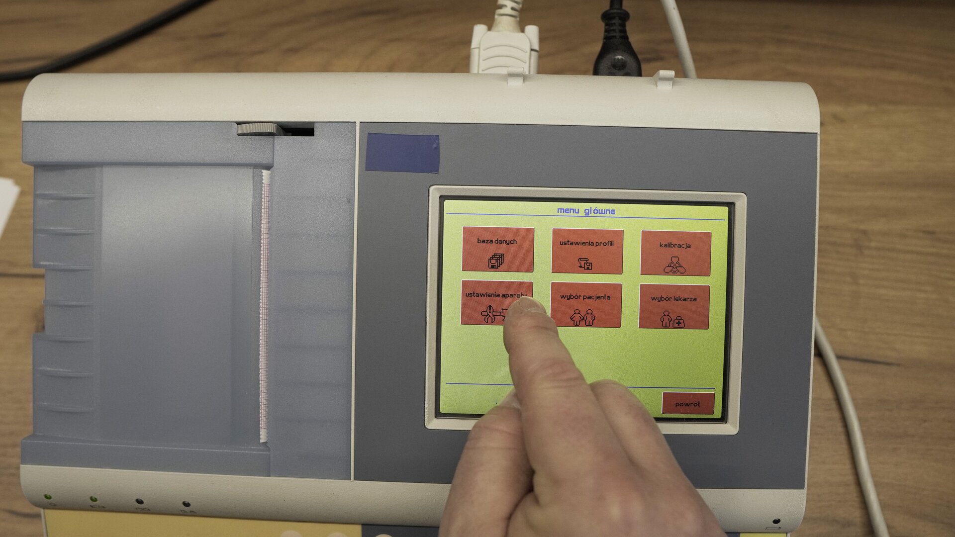 Na zdjęciu technik wybiera na klawiaturze ekranowej spirometru przycisk Ustawienia aparatu,
