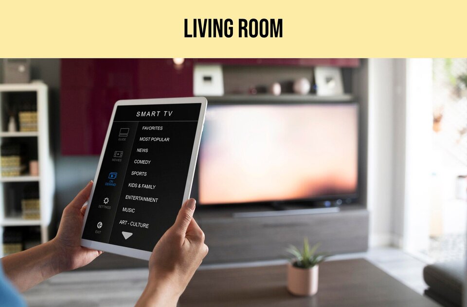 Ilustracja przedstawia z lewej strony dwie dłonie trzymające tablet. Na ekranie tabletu widoczne są napisy w języku angielskim: SMART TV, FAVORITES, MOST POPULAR, NEWS, COMEDY, SPORTS, KIDS &amp; FAMILY, ENTERTAINMENT, MUSIC, ART - CULTURE. W tle widoczne jest wyposażenie pokoju z dużym telewizorem. U góry ilustracji widoczny jest napis w języku angielskim: LIVING ROOM.