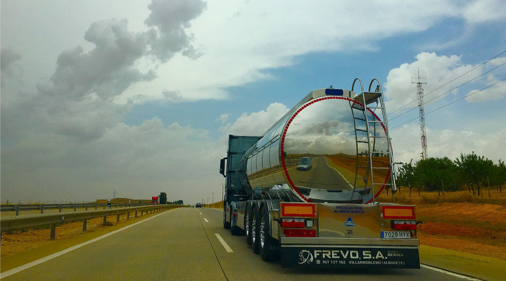 Na zdjęciu widoczny jest pojazd cysterna o podwoziu cylindrycznym. Cysterna widoczna jest od tyłu. Pojazd porusza się po drodze publicznej. Beczka cysterny jest o przekroju elipsy. Kolor beczki jest stalowy. Z tyłu beczki zamontowana jest drabina. 