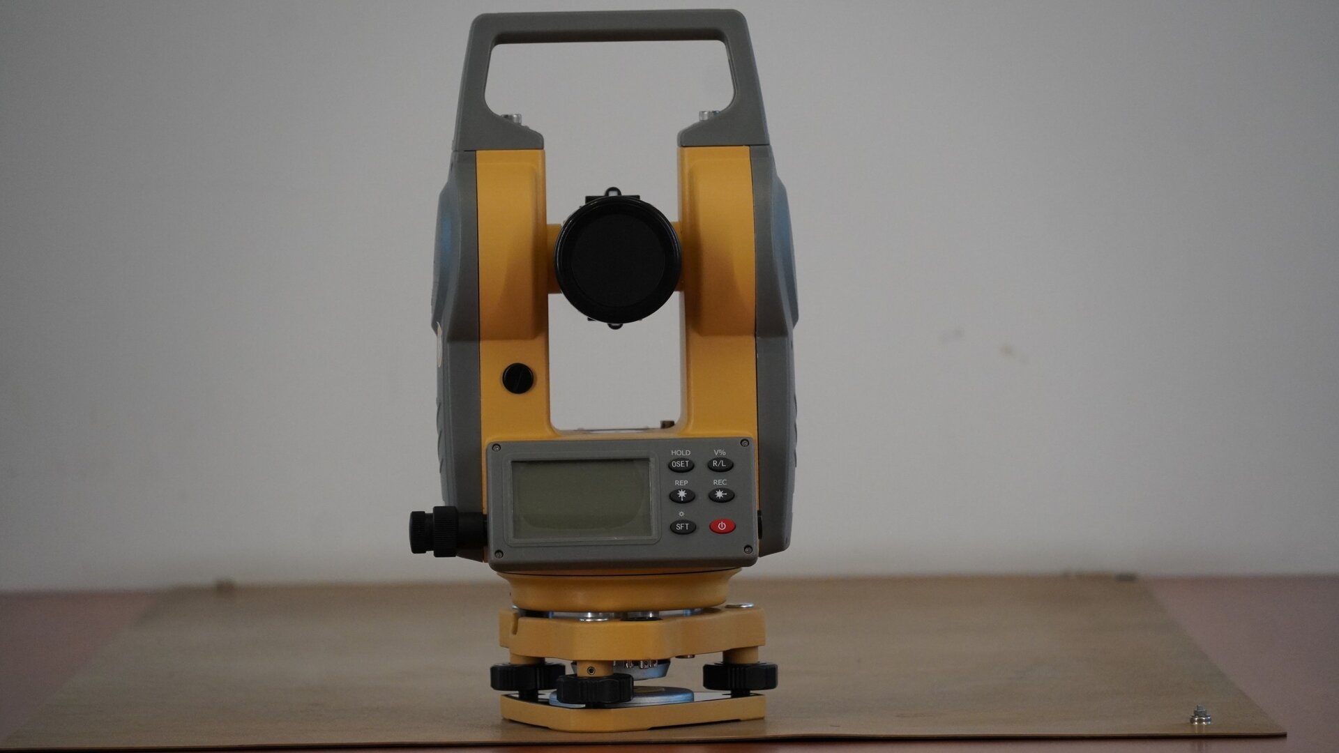 Na zdjęciu przedstawiono teodolit od strony obiektywu. Urządzenie posiada trójkątną podstawę w formie płytki sprężynującej. W każdym jej rogu znajduje się śruba poziomująca. Na śrubach osadzona jest spodarka, czyli podstawa instrumentu. W spodarce mieści się śruba dociskowa, a na spodarce okrągła alidada, czyli korpus urządzenia. Na nim zaś znajdują się pokrętła leniwki alidady i leniwki lunety oraz zacisk alidady i lunety. Konstrukcję instrumentu uzupełnia prostokątna rama z uchwytem w górnej części, wewnątrz została osadzona luneta. Pod obiektywem znajduje się wyświetlacz z przyciskami.