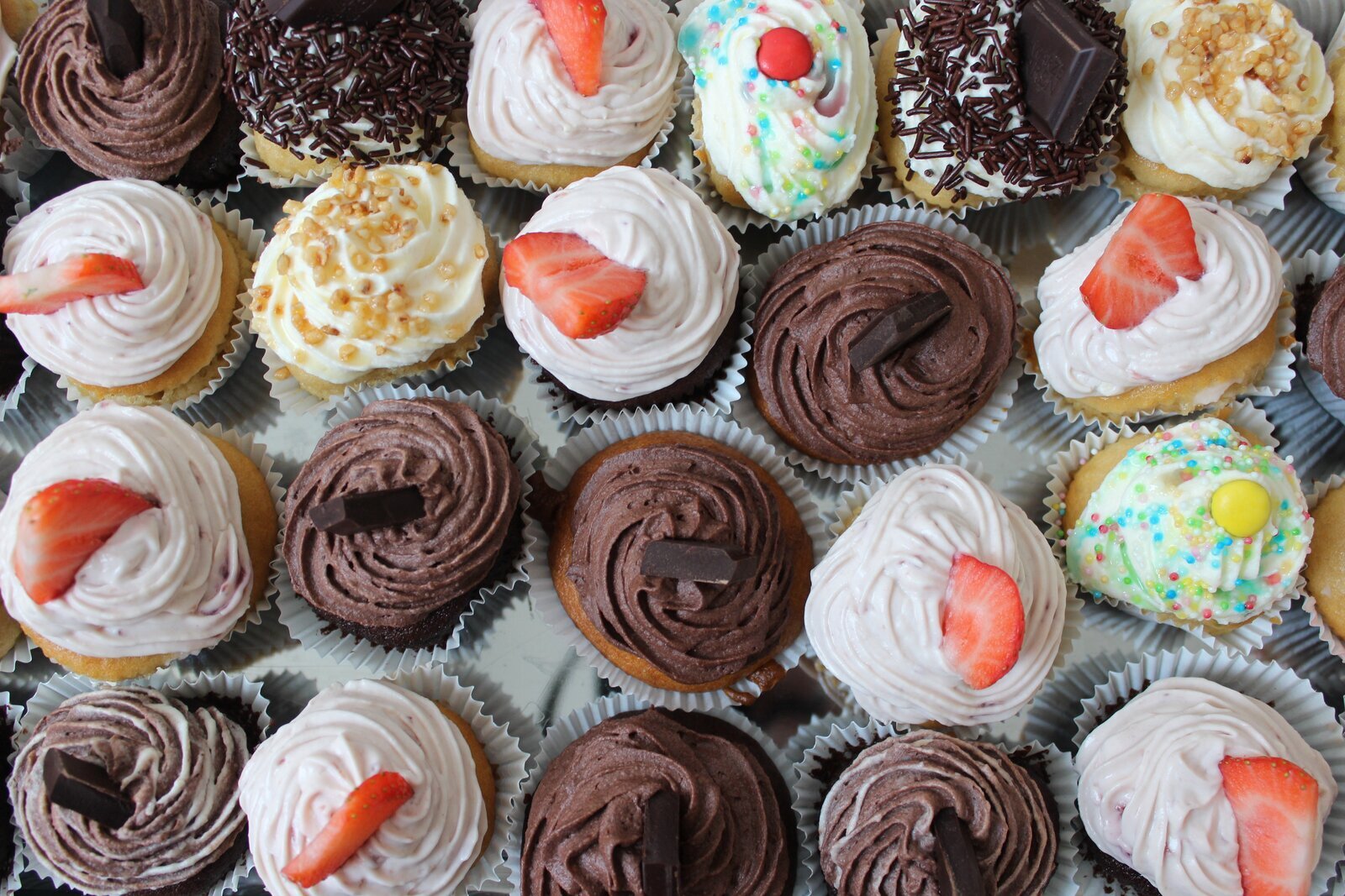 Ilustracja przedstawia muffiny, udekorowane owocami, kawałkami czekolady i posypkami.