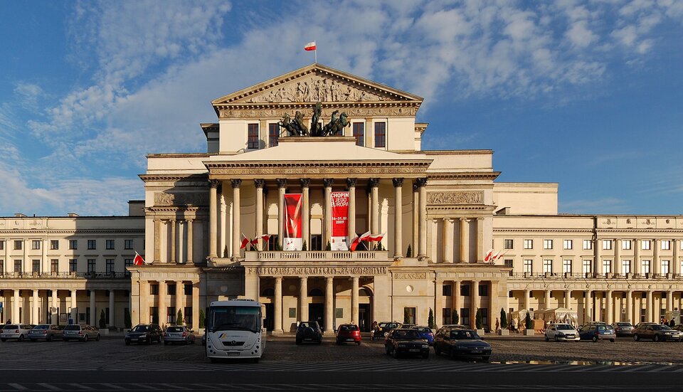 Ilustracja przedstawia monumentalny budynek na placu. Bryła budynku podzielona jest na trzy części, centralną oraz dwa boczne skrzydła. Wszystkie części składają się z trzech kondygnacji. W centralnej kondygnacja pierwsza, znajdująca się przy ziemi i najszersza, to wysunięty portyk z kolumnadą, złożoną z czterech kolumn w stylu doryckim. Na kolumnadzie umieszczony został fryz z gzymsem oraz balustradą. Na drugiej kondygnacji znajduje się kolumnada z dziesięcioma kolumnami w stylu korynckim, zwieńczone ozdobnym belkowaniem. Gzyms kończy dach z cokołem oraz rzeźbą.  Druga kondygnacja jest wysunięta przed lico budynku, jednak nie przed portyk. Zakończenie części środkowej stanowi płaskorzeźba Popiersie Anakreonta i trzy muzy. Rzeźbą zdobiącą dach z cokołem jest natomiast kwadryga, czterokonny rydwan powożony przez boga Apolla. Na trzeciej kondygnacji znajdują się natomiast dwa symetryczne wobec głównej pionowej osi budynku tarasy. Pośrodku umiejscowiona jest ściana z drzwiami. Po obu strona otworu drzwiowego umieszczone są po trzy okna, zwieńczone fryzem z reliefowymi girlandami kwiatowym.