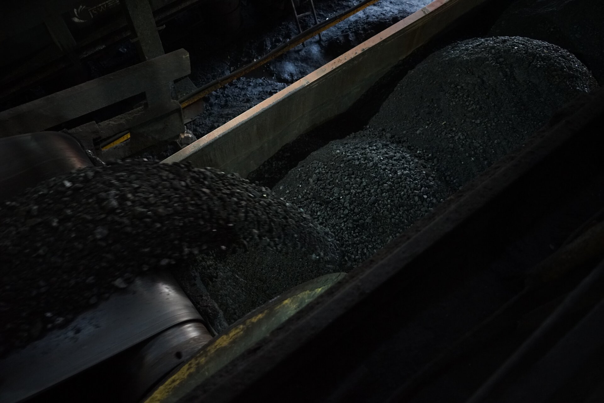 Na zdjęciu widać nasypywarkę podczas załadunku węgla. Po lewej stronie zdjęcia znajduje się nasypywarka. Nasypywarka przypomina przenośnik taśmowy. Na taśmie osadzonej na rolce znajduje się rozdrobniony węgiel. Nasypywarka znajduje się nad wagonem transportowym. Wagon jest częściowo załadowany drobnorozdrobnionym węglem. Węgiel zrzucany jest z nasypywarki do wagonu. Nasypuywarki znajduje się w budynku przemysłowym.Poniżej zdjęcia widoczny jest przycisk multimedialny z nagraniem audio. Treść nagrania jest zgodna z tytułem zdjęcia.