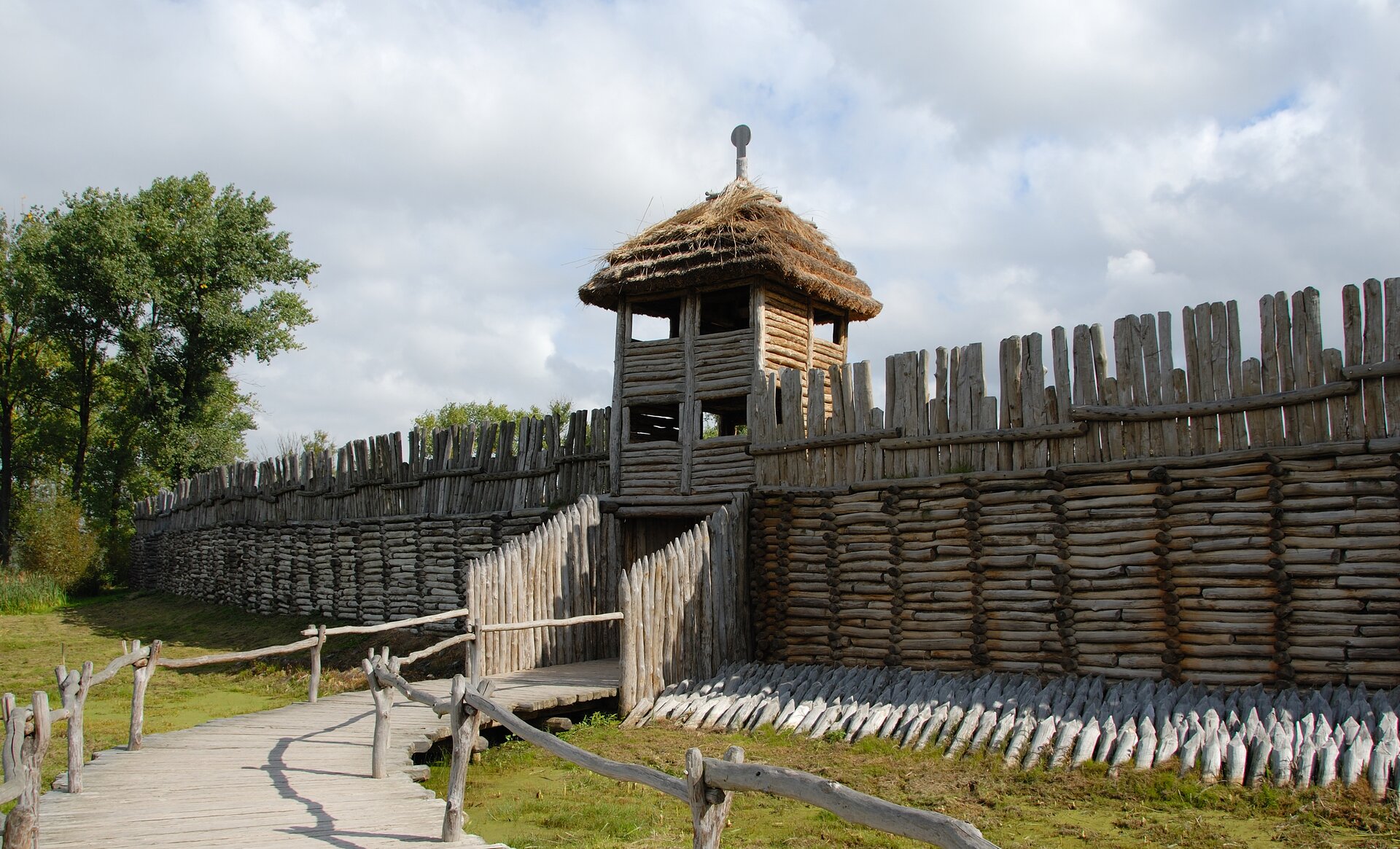 Fotografia barwna przedstawiająca drewnianą bramę zrekonstruowanej osady w Biskupinie. Color photography depicting the wooden gate of the reconstructed settlement in Biskupin.