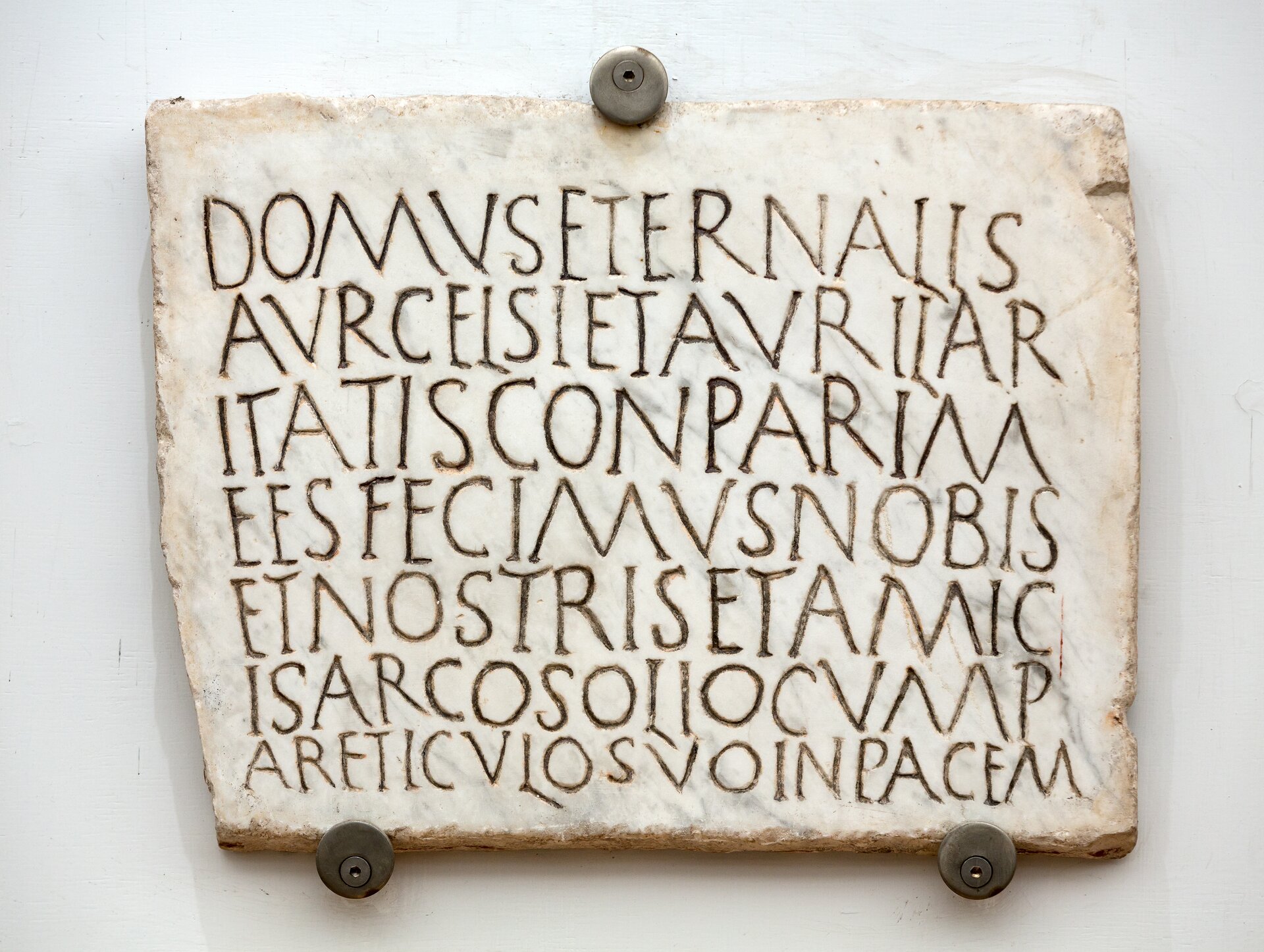 Ilustracja przedstawia płytę nagrobną wykonaną z białego marmuru. Znajdująca się na niej inskrypcja w języku łacińskim jest pisana bez przerw między wyrazami. Litery są duże i wyraźne.