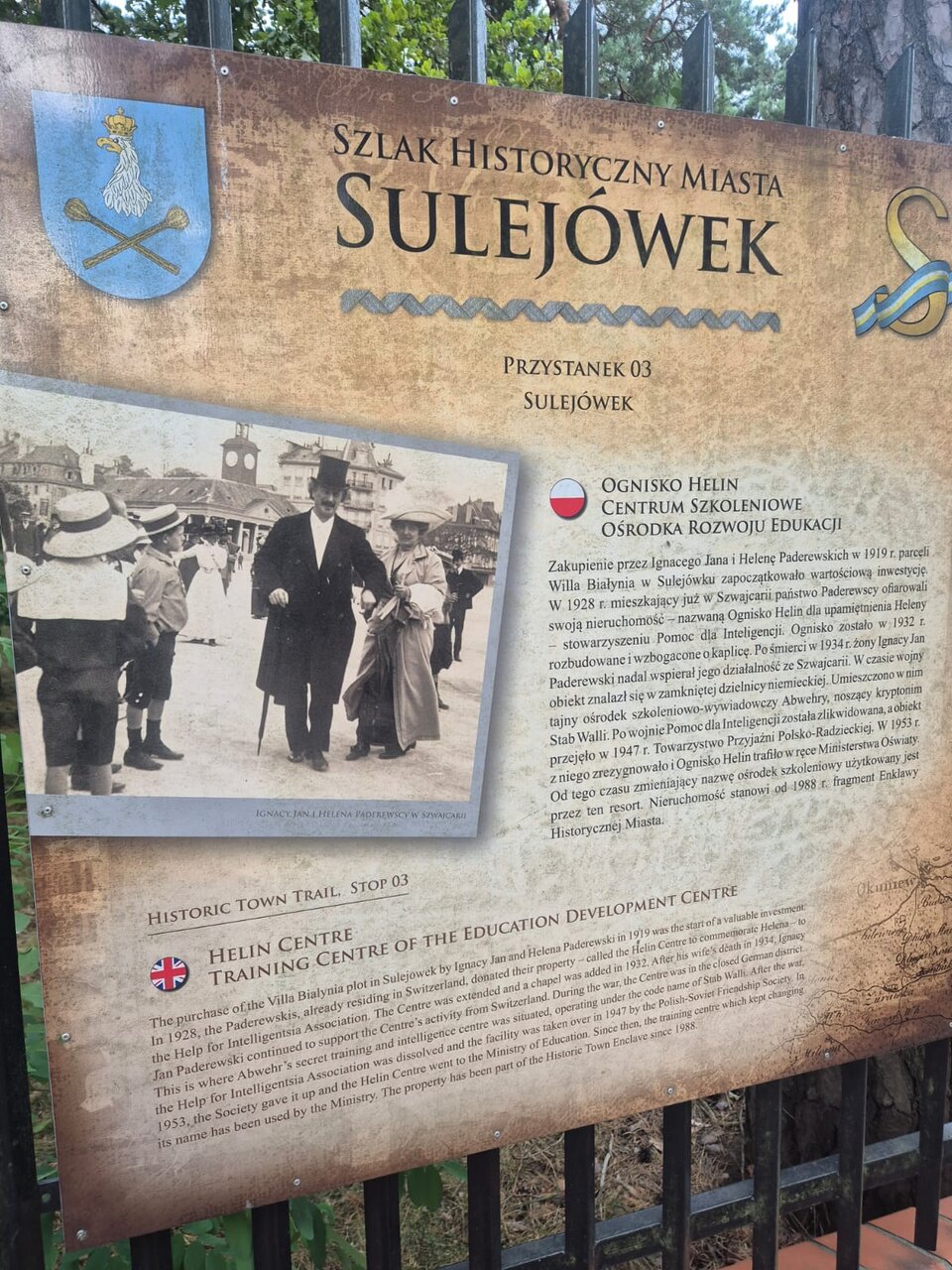 Ilustracja przedstawia jedną z tablic informacyjnych Szlaku Historycznego Miasta Sulejówek. Jest to trzeci przystanek pod nazwą "Ognisko Helin". Obecnie tablica jest umieszczona na na ogrodzeniu ośrodka szkoleniowego w Sulejówku. Przedstawia zdjęcie Paderewskiego przemierzającego ulicę w otoczeniu innych osób oraz informacyjny tekst dwujęzyczny: polski i angielski.