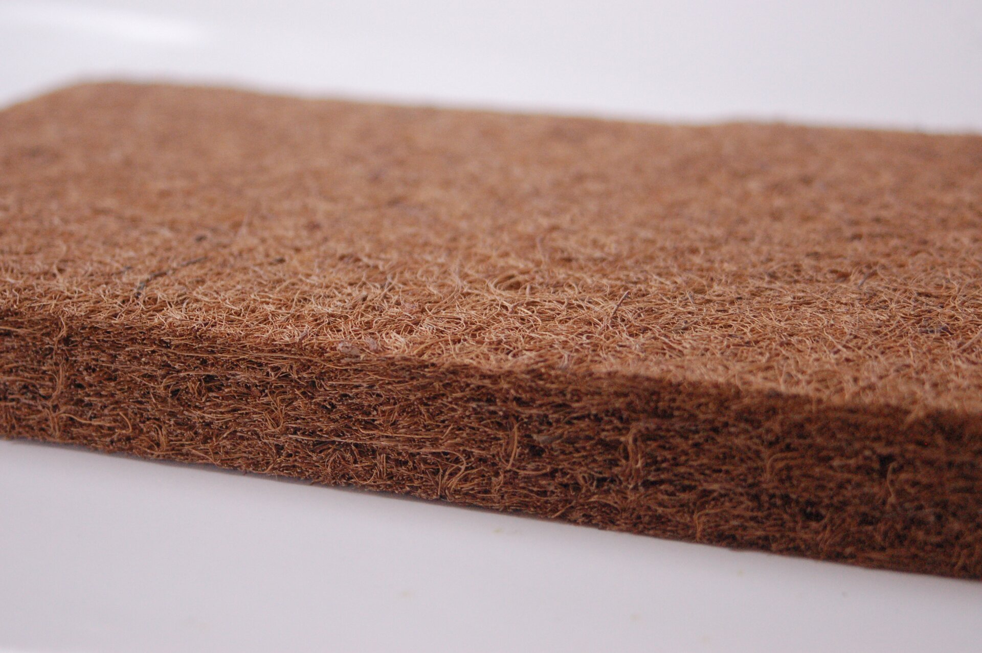 Zdjęcie przedstawia włókno kokosowe zbite w brązowy płaski prostopadłościan o niewielkiej grubości, widziany z boku w zbliżeniu.