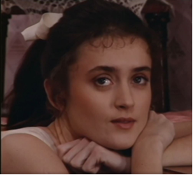 Zdjęcie przedstawia młodą kobietę. Opiera głowę na skrzyżowanych rękach, przed gdzieś w górę, ma długie, ciemne włosy z białą kokardą.