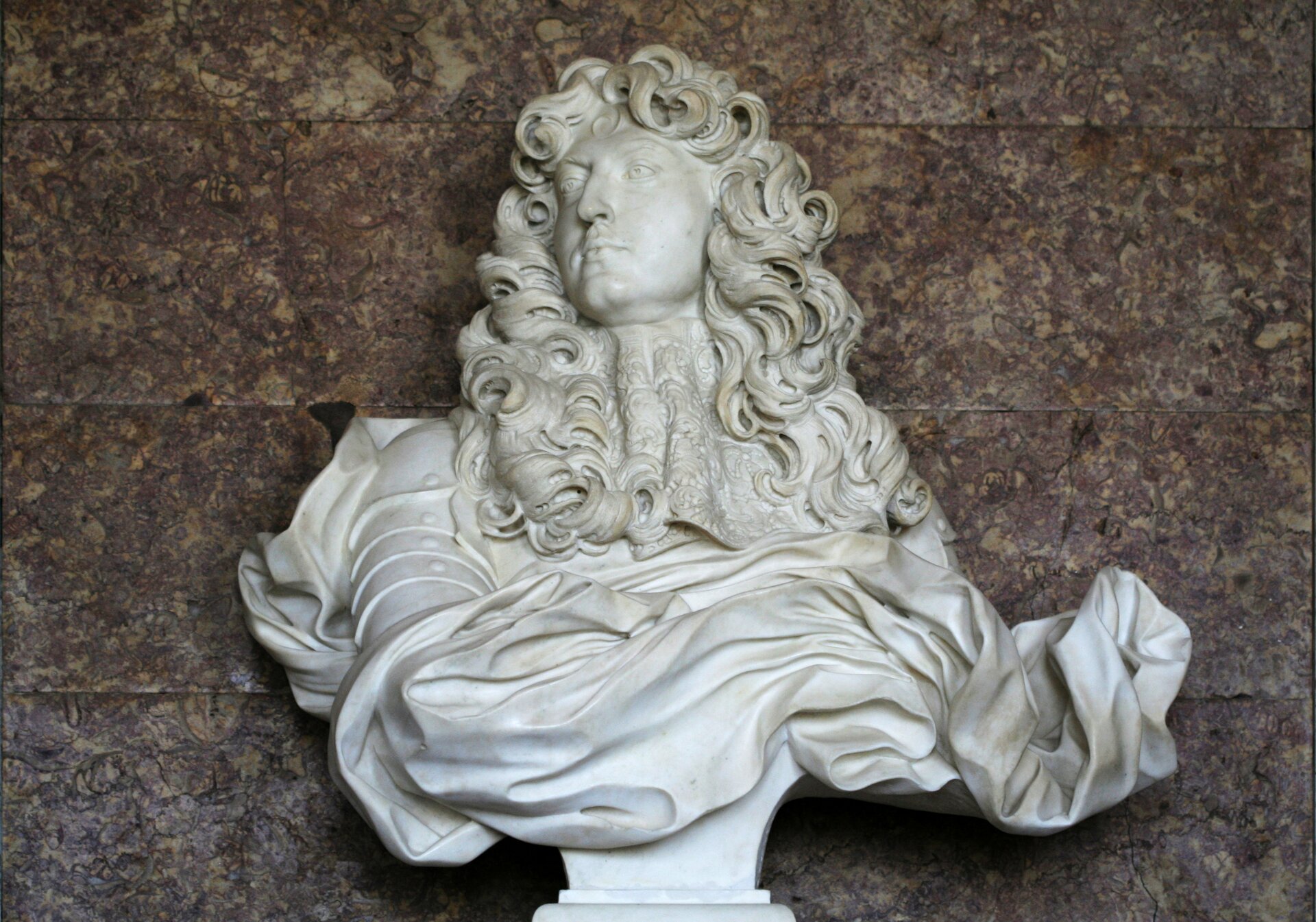 Ilustracja przedstawia rzeźbę „Popiersie Ludwika XIV” autorstwa Gian Lorenzo Berniniego. Wykonane z białego marmuru dzieł ukazuje mężczyznę w średnim wieku z długimi, kręconymi włosami spływającymi na ramiona. Postać ubrana jest w zbroję, którą okrywa dynamicznie wyrzeźbiona, pofałdowana draperia. Pod szyją znajduje się misternie wykonany, koronkowy żabot. Głowa mężczyzny zwrócona jest w prawą stronę. Popiersie wyrzeźbione jest na zwężającym się ku dołowi postumencie. 