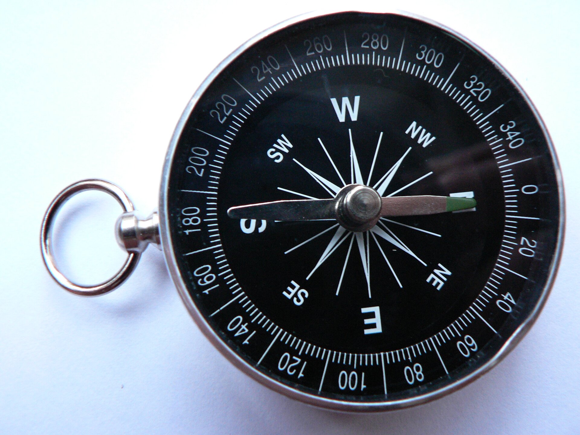 Zdjęcie przedstawiające okrągły, metalowy kompas z okrągłą zawieszką. Ma czarną tarczę z liczbami od 0 do 340 oraz litery oznaczające kierunki świata, a także dwie podłużne wskazówki.