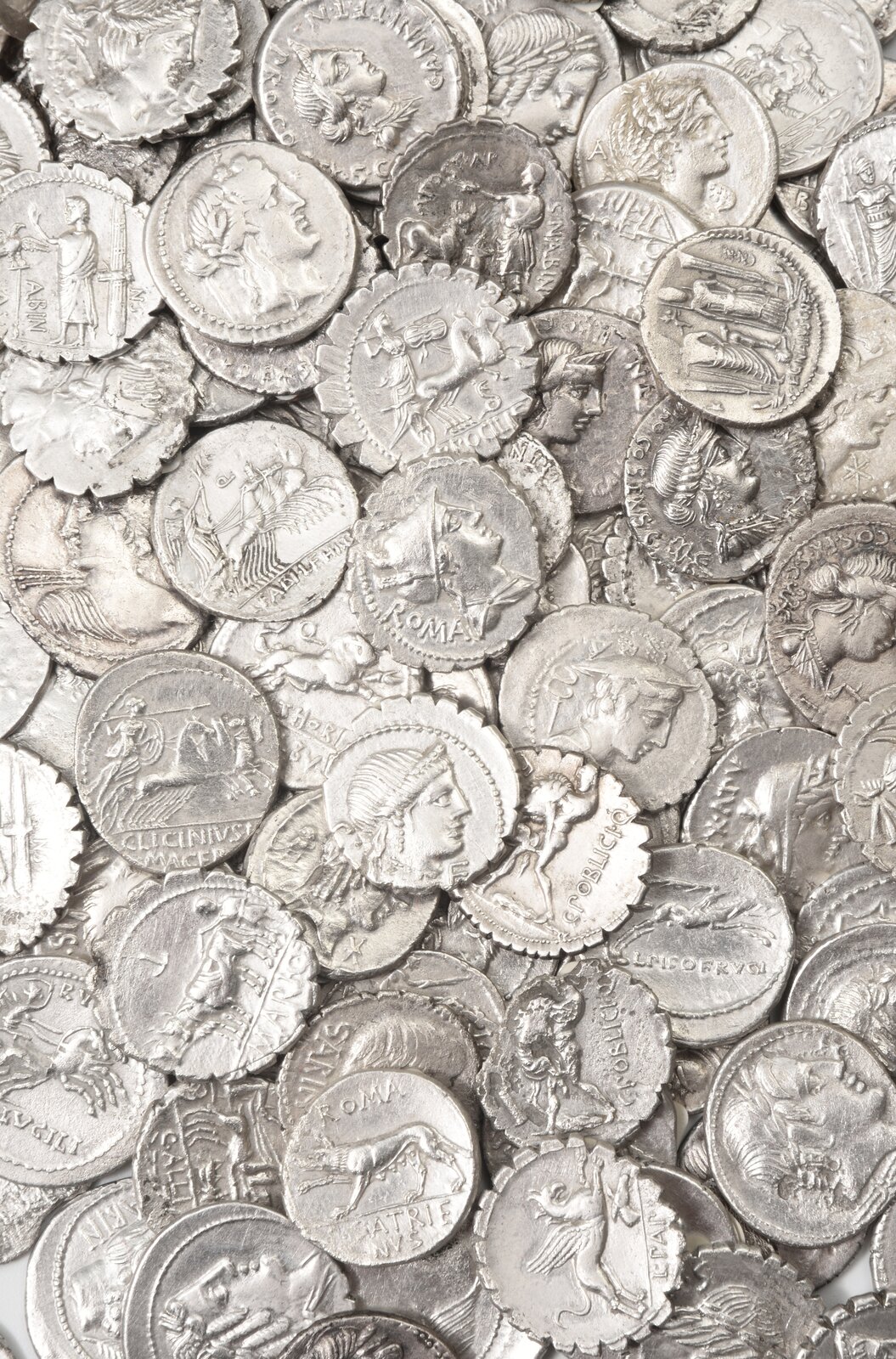Ilustracja przedstawia stos srebrnych monet. Monety przedstawiają starożytne postacie oraz motywy zwierzęce.