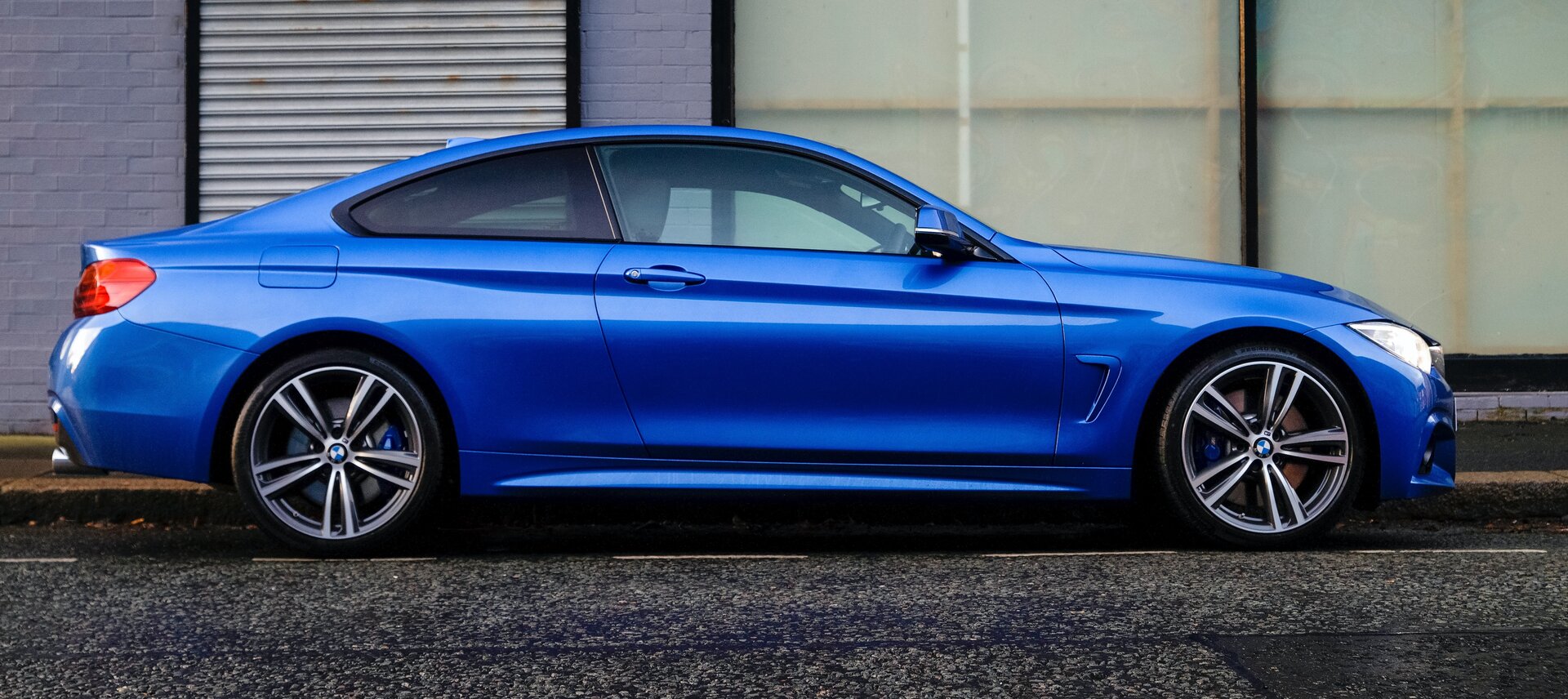 Zdjęcie przedstawia niebieski samochód osobowy, stojący na jezdni, zwrócony w prawą stronę. 