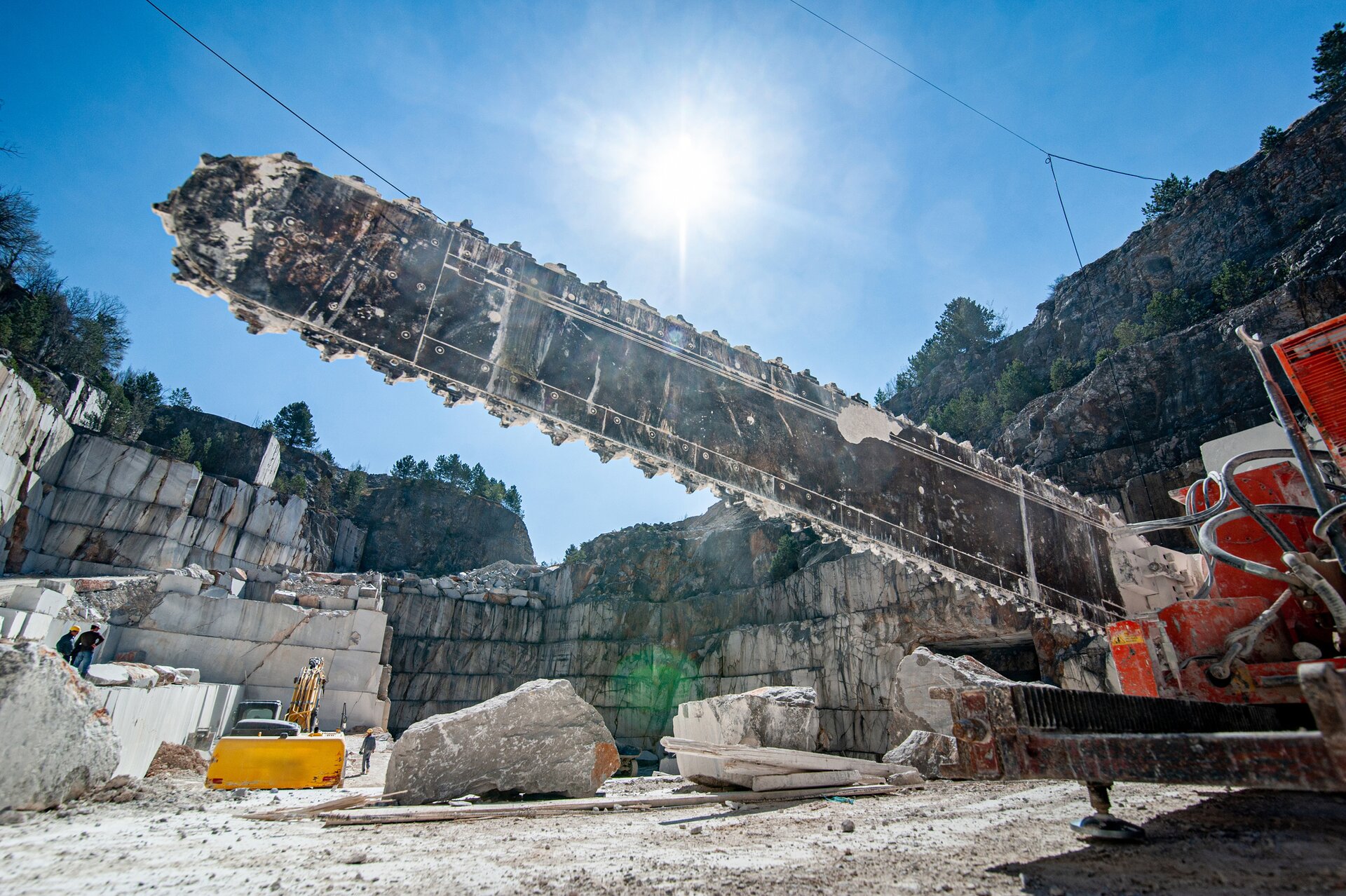 Zdjęcie przedstawiające cięcie kamienia za pomocą traka łańcuchowego. Ta duża maszyna znajduje się w kamieniołomie. Wokół miecza traka nawinięty jest łańcuch.