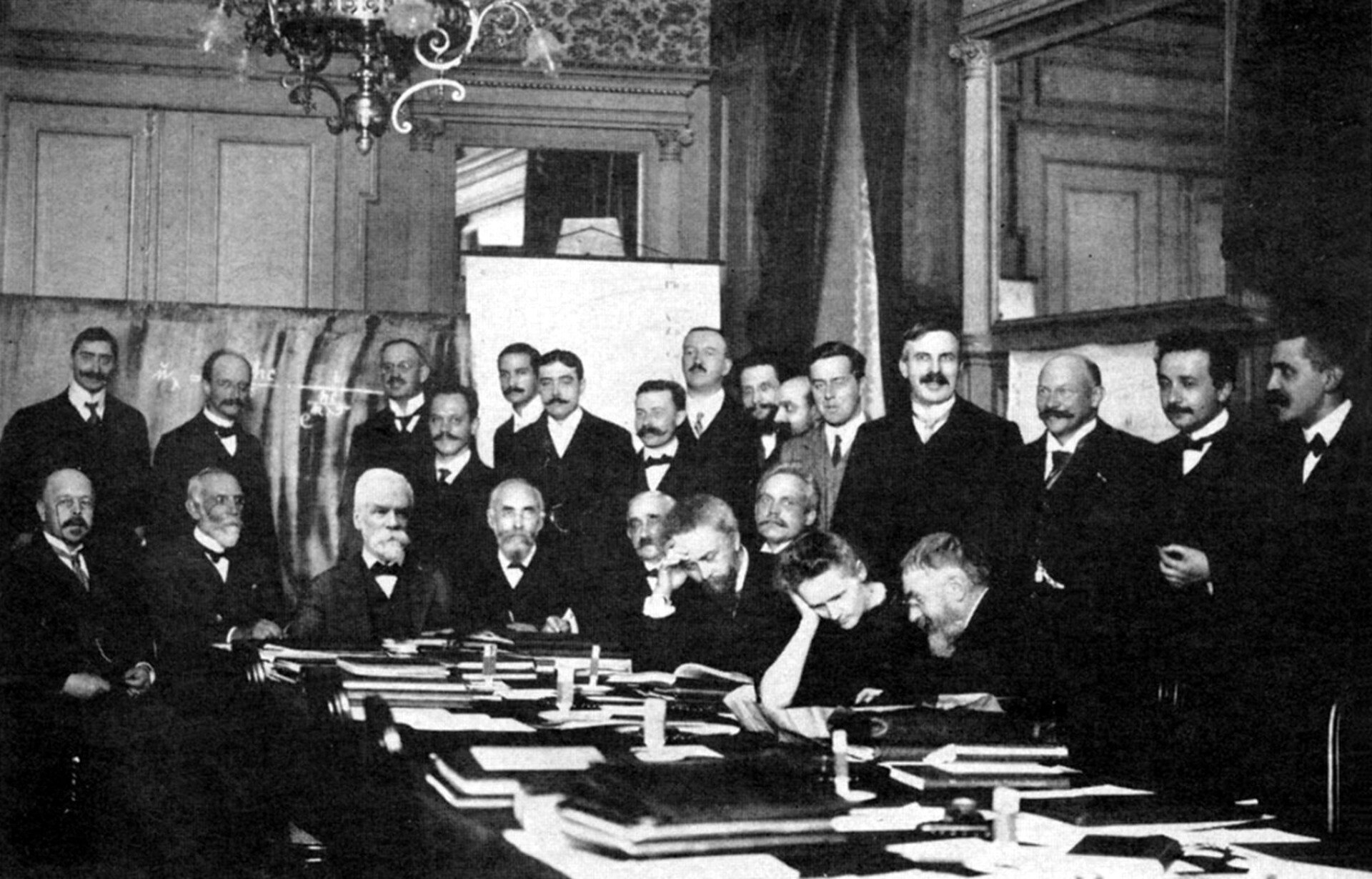 Fotografia czarno-biała przedstawiająca uczestników Pierwszego Kongresu Solvaya, który odbył się w Brukseli w 1911 r.  Przy stole od lewej do prawej siedzą kolejno: Walther Nernst, Marcel Brillouin, Ernest Solvay, Hendrik Lorentz, Emil Warburg, Jean Perrin, Wilhelm Wien, Maria Skłodowska-Curie, Henri Poincaré. Za siedzącymi stoją od lewej: Robert Goldschmidt, Max Planck, Heinrich Rubens, Arnold Sommerfeld, Frederick Lindemann, Maurice de Broglie, Martin Knudsen, Friedrich Hasenöhrl, Georges Hostelet, Edouard Herzen, James Hopwood Jeans, Ernest Rutherford Rutherford, Heike Kamerlingh Onnes, Albert Einstein, Paul Langevin.
