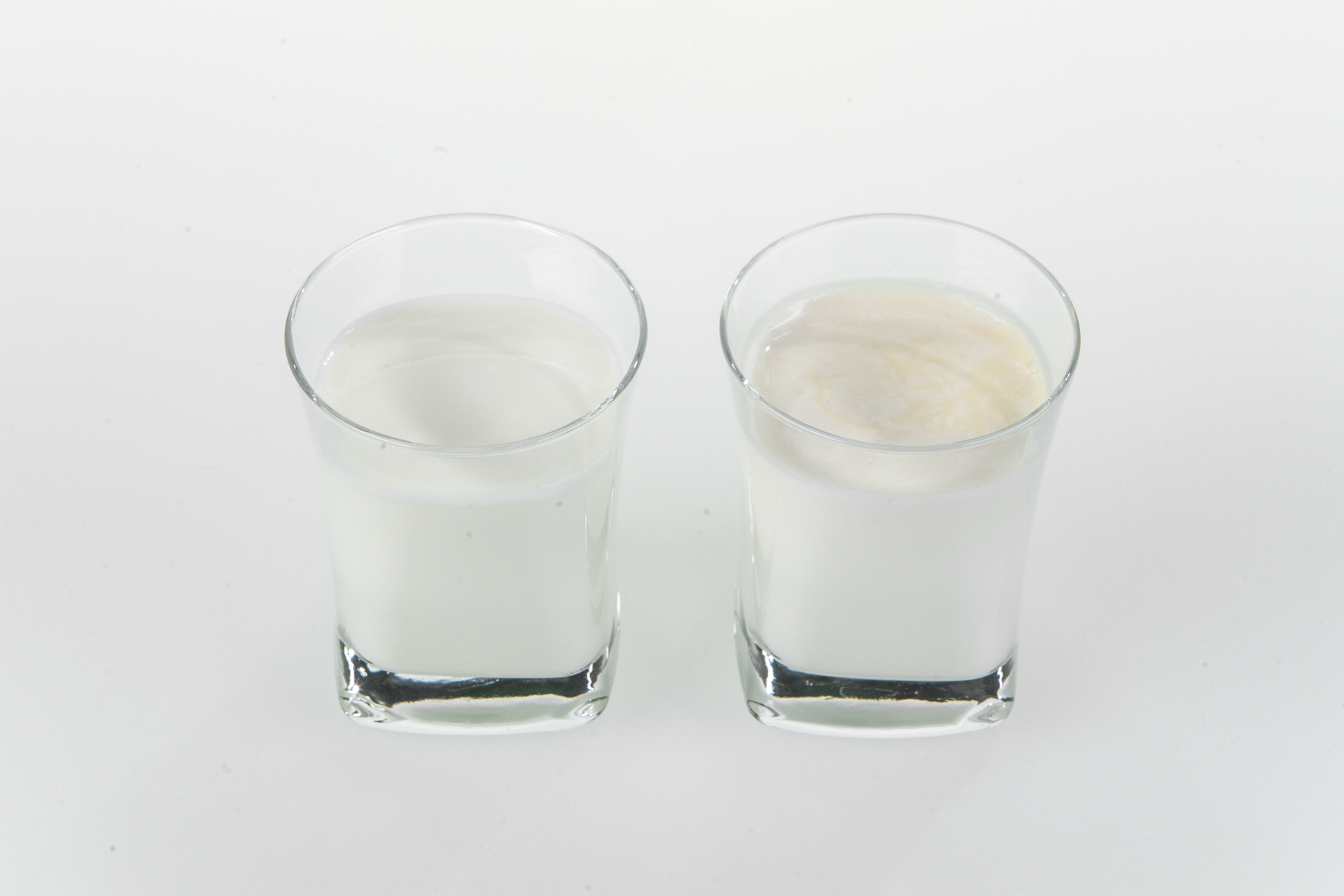Na zdjęciu przedstawiono dwie szklanki, w jednej znajduje się mleko, a w drugiej mleko na którego powierzchni zaczęła zbierać się śmietana. Szklanki są przeźroczyste. W szklance, w której zaczęła zbierać się śmietana widoczny jest żółtawy kożuch na powierzchni cieczy.