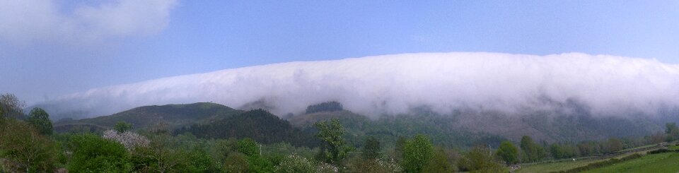 Zdjęcie przedstawia pasmo górskie przykryte chmurami. Chmury przybierają kształt kopuły. Nad chmurami jest niebieskie niebo. 
