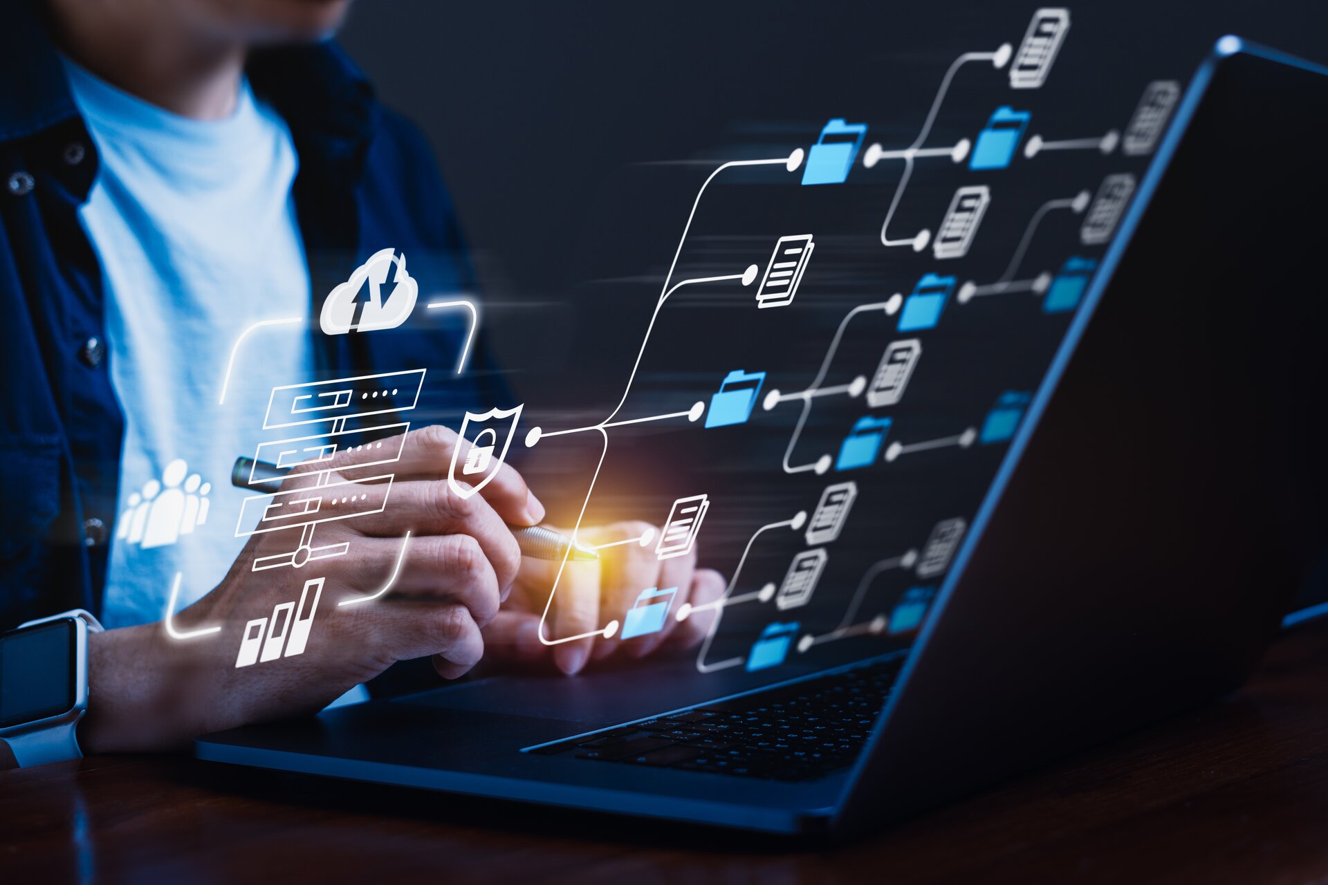Zdjęcie przedstawia mężczyznę piszącego na laptopie. Z ekranu laptopa wychodzą połączone ze sobą ikony przedstawiające zapisywanie plików w różnych folderach oraz udostępnianie ich.