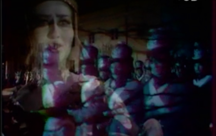 Fotografia przedstawia nakładające się na siebie dwa obrazy. Po lewej stronie, u góry ukazana jest twarz kobiety w sile wieku. Postać ukazuje trzy czwarte twarzy zwróconej w jej lewą stronę. Kobieta ma gładkie czoło, ciemne, zmarszczone brwi, lekko zwężone oczy, niewielki nos i wydatne, otwarte usta. Patrzy przed siebie. Na głowie ma hełm. Po prawej stronie, u dołu ukazani są żołnierze stojący w szyku. Mężczyźni są umundurowani. W dłoniach trzymają broń.