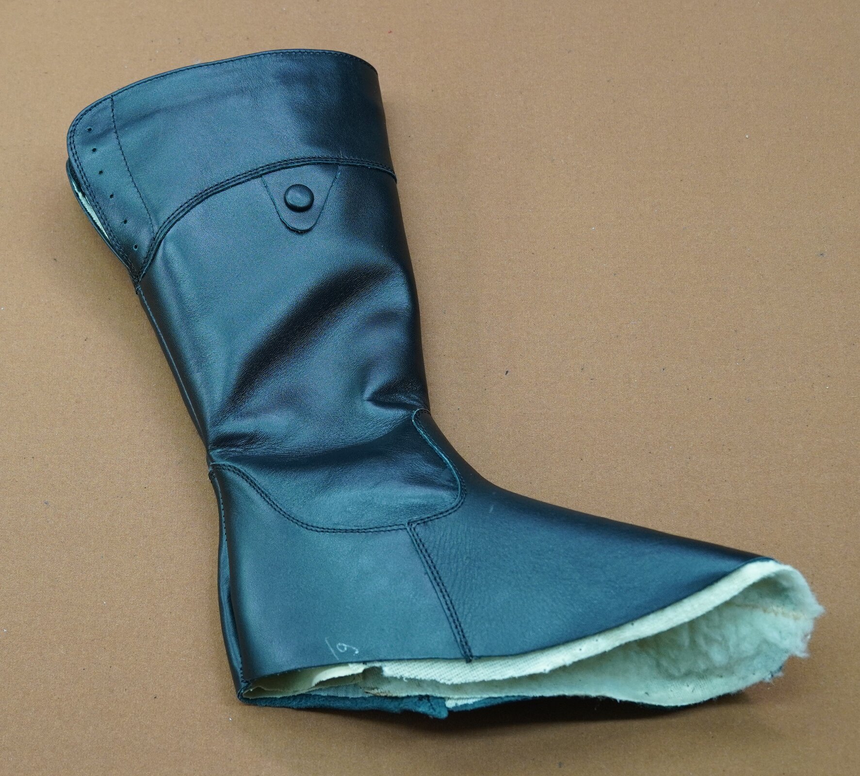 Zdjęcie przedstawia skórzanego kozaka z wysoką cholewką. But nie ma podeszwy.