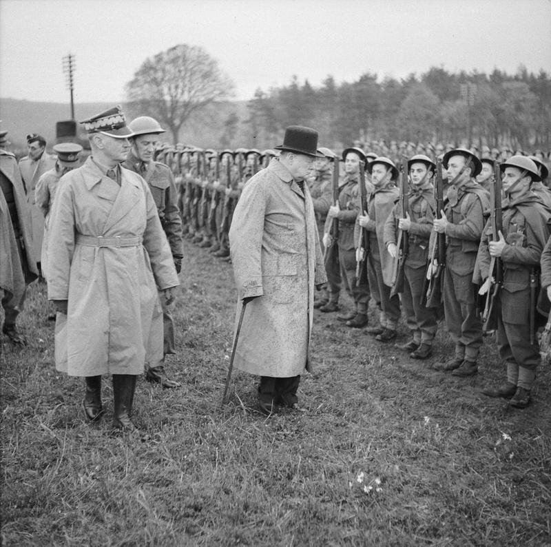 Zdjęcie przedstawia polskich żołnierzy z oddziałów I Korpusu. Żołnierze stoją na baczność, w rzędach, są uzbrojeni w karabiny. Wzdłuż pierwszego rzędu przechodzą Winston Churchill i generał Władysław Sikorski oraz inni oficerowie.
