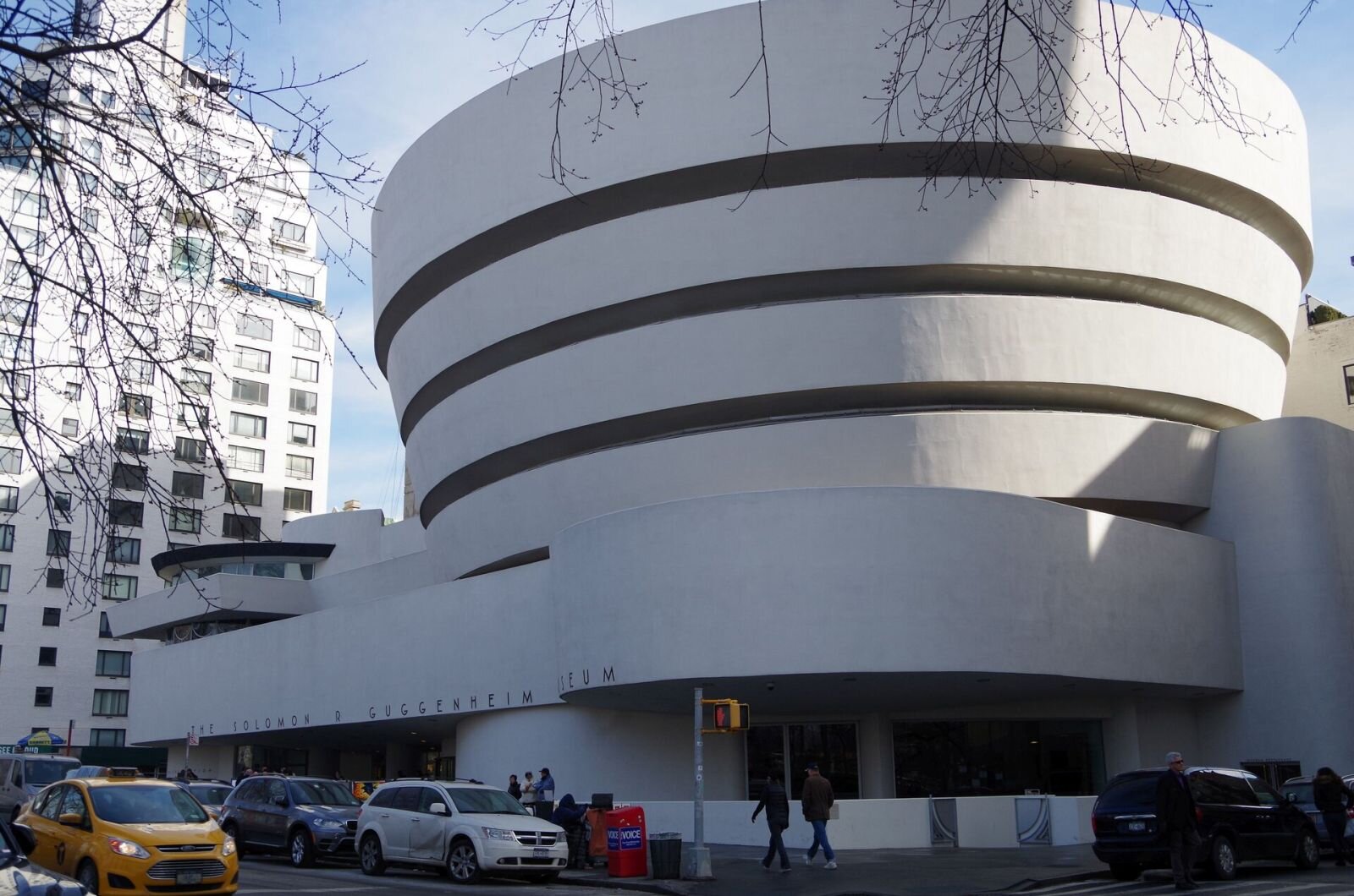 Ilustracja przedstawia budynek MuzeumGuggenheima w Nowym Yorku, zaprojektowany przez Franka Lloyda Wrighta (czyt. lojda łrajta). Nowoczesny budynek, przypomina zwiniętą jasną wstęgę, zwęża się lekko ku dołowi. Spiralny kształt posiada u dołu ramię, na którym widnieje nazwa muzeum. W tle znajduje się wieżowiec. 