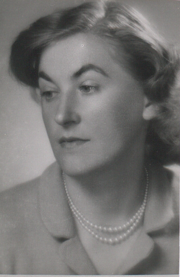 Zdjęcie przedstawia twarz młodej kobiety. Kobieta jest jasnowłosa. Ma pociągłą twarz, spiczasty nos i ciemną oprawę oczu. Jej włosy są falujące półdługie, sięgające ramion. Kobieta ubrana jest w żakiet. Na jej szyi wisi podwójny sznur pereł.