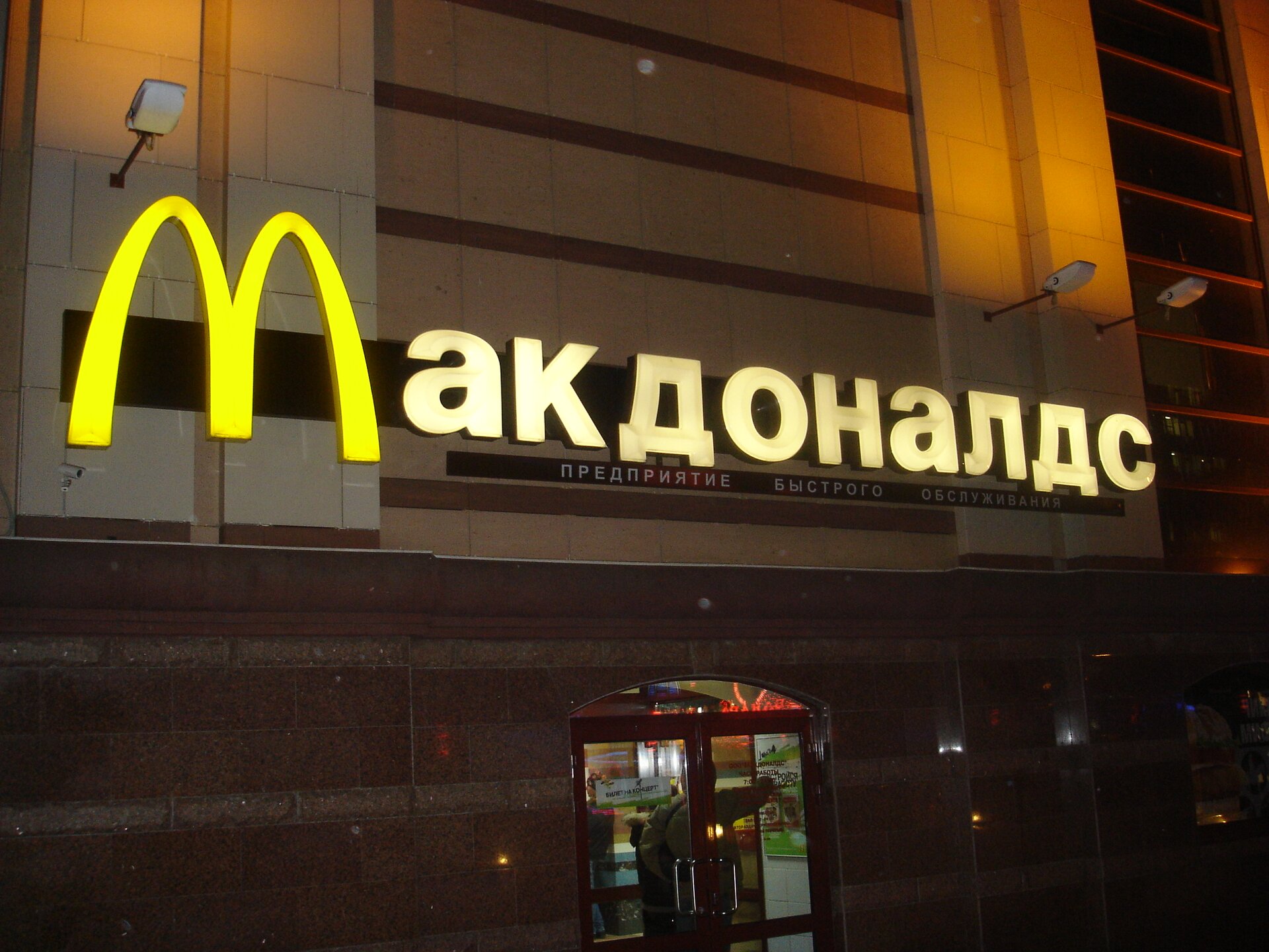 Zdjęcie przedstawia wejście do restauracji. Neon. Nazwa firmy McDonad's zapisana cyrylicą.